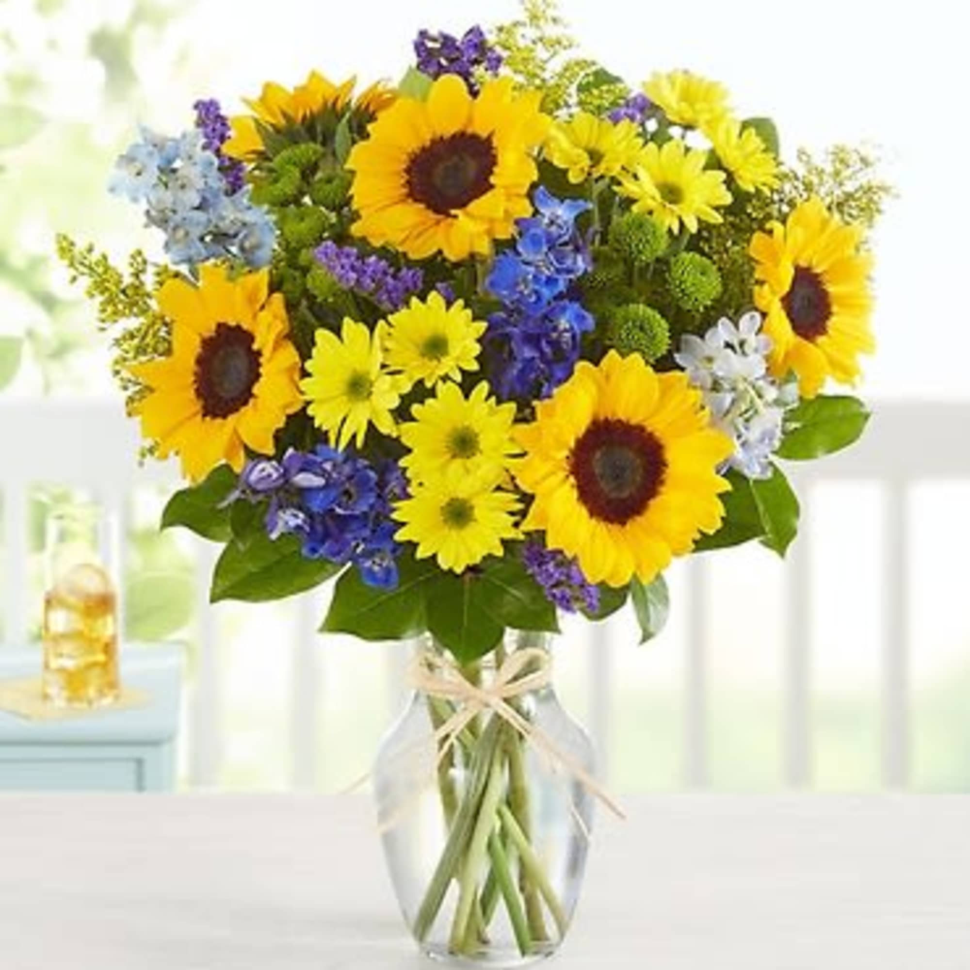 Bouquet of sunflowers and mixed blue and yellow flowers in a glass vase
