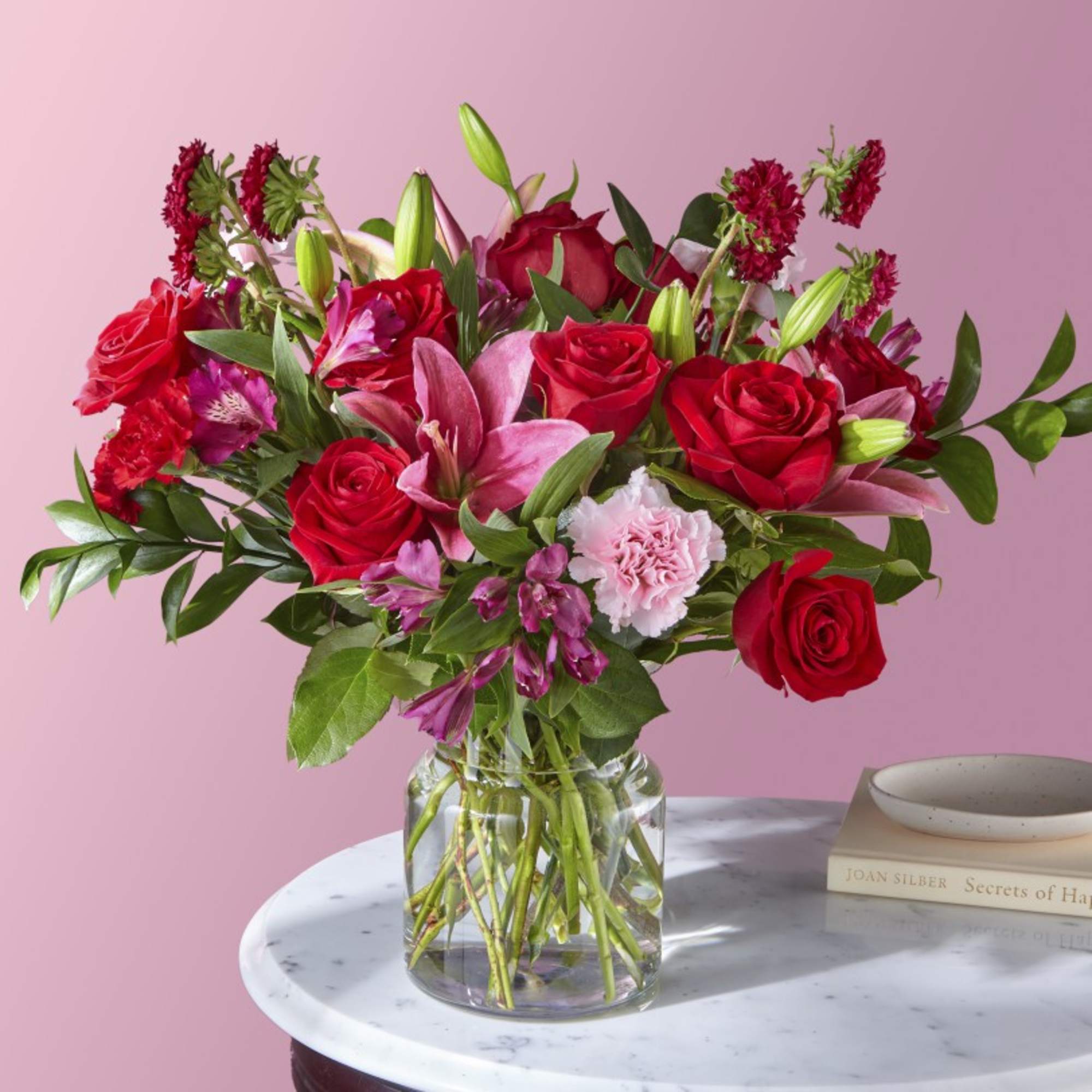 Bouquet of red roses, pink lilies, and carnations in a clear glass vase
