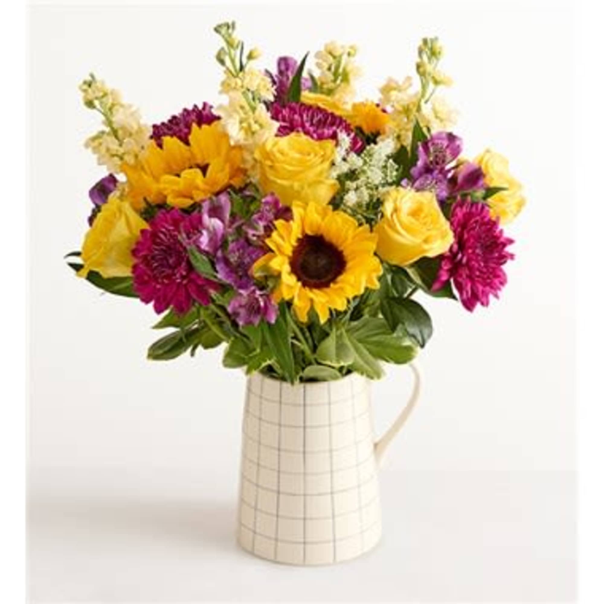 Mixed bouquet of yellow and magenta flowers in a checked ceramic pitcher