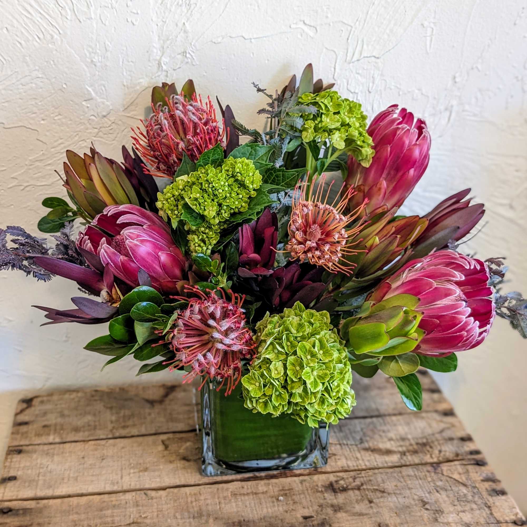 Pink protea and green hydrangeas in a square glass vase