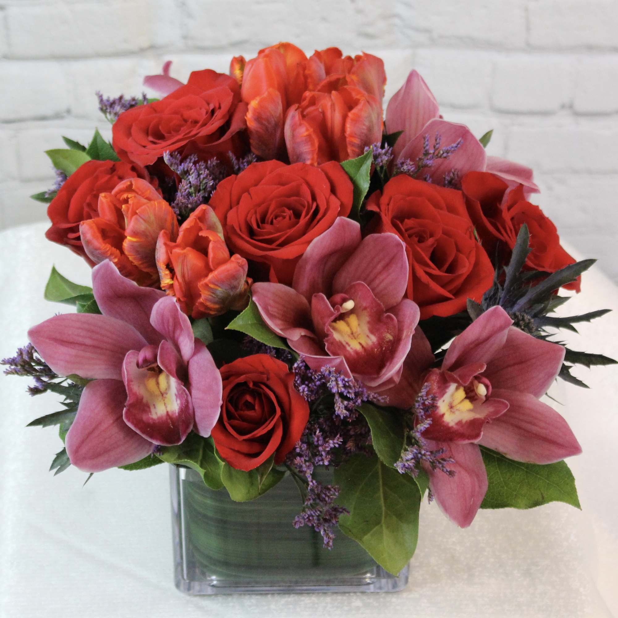 Bouquet of red roses and pink orchids in a square glass vase