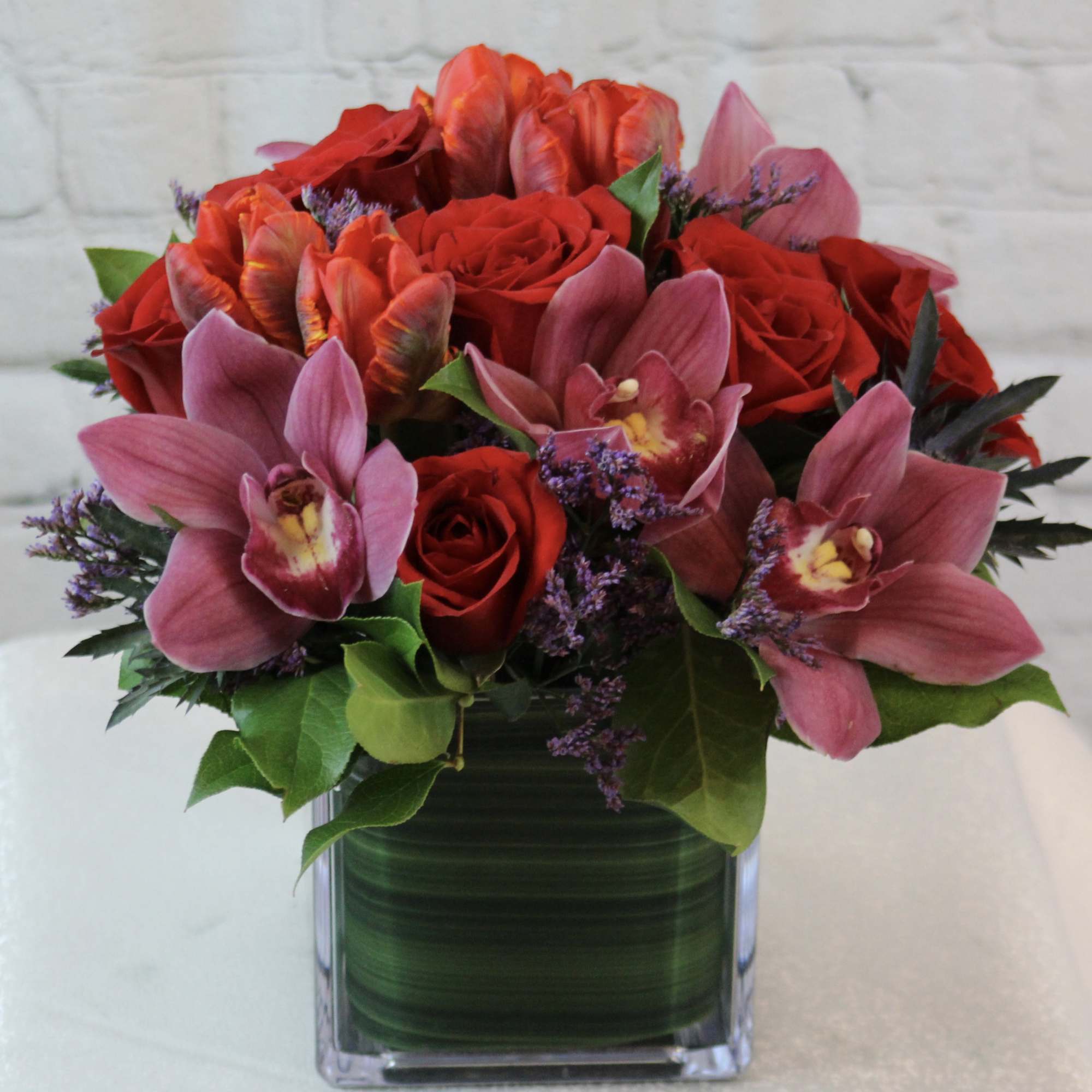 Red roses and pink orchids arranged in a square glass vase