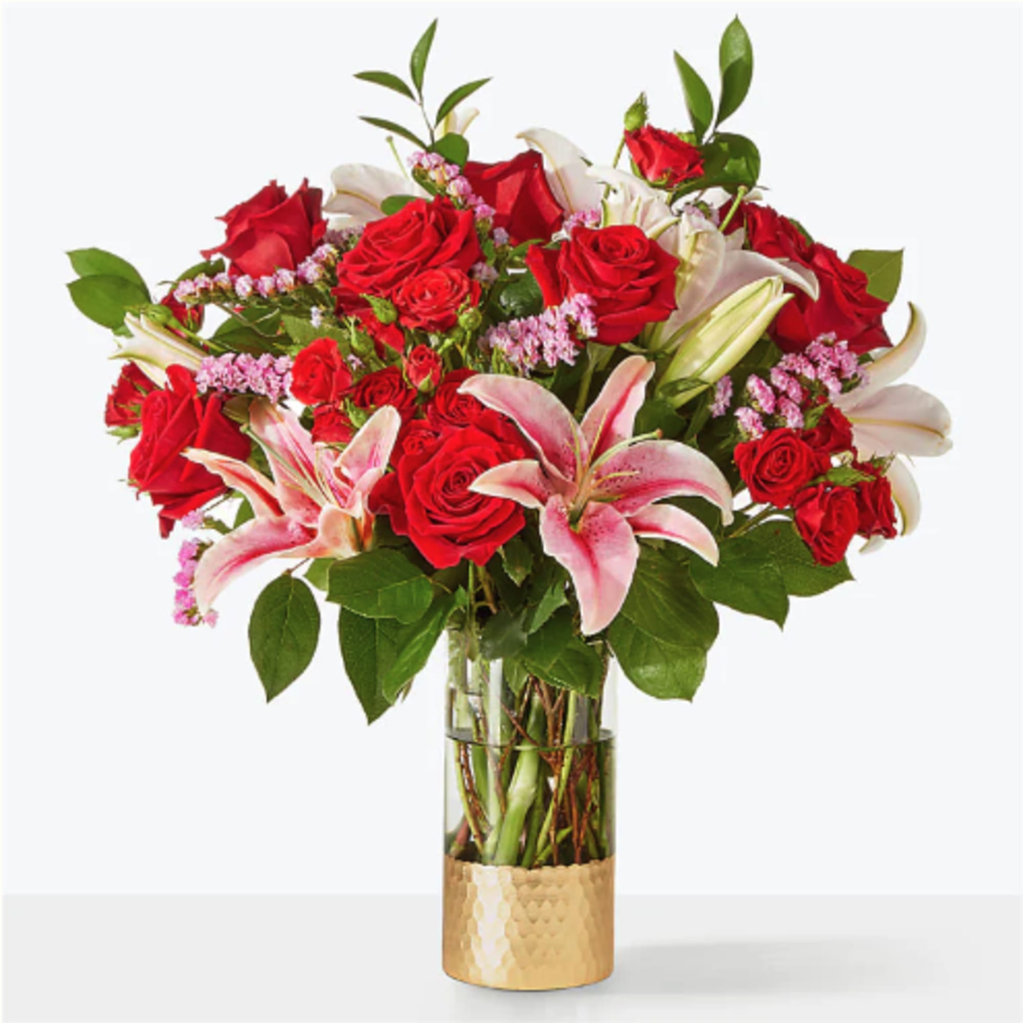 Red roses and pink lilies arranged in a glass vase with a gold base