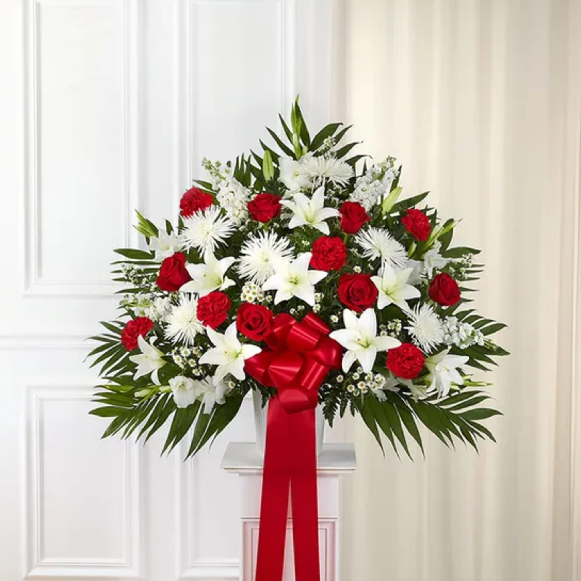 Standing floral spray with red roses and white lilies, tied with a red ribbon