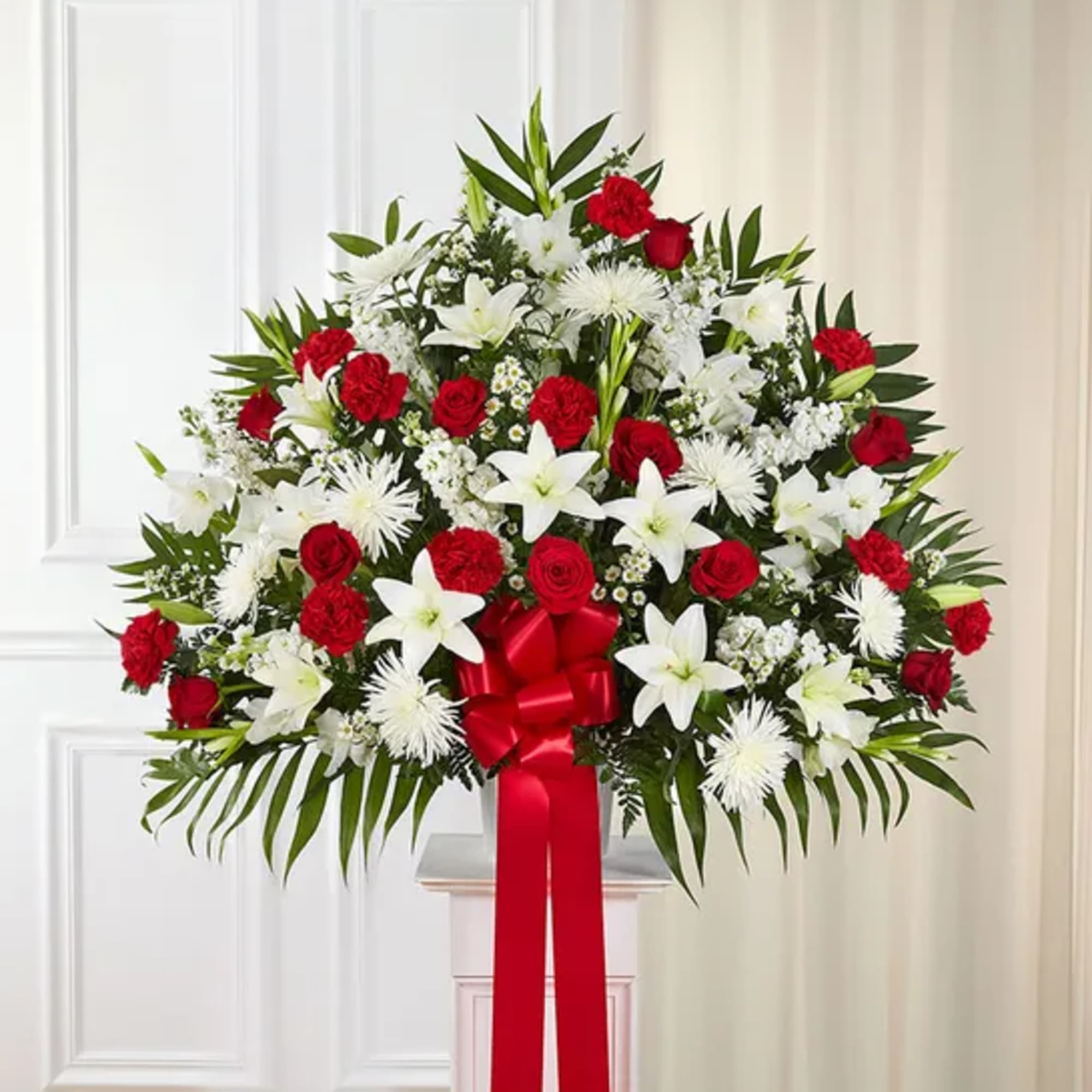 Red roses and white lilies in a standing spray with a red ribbon