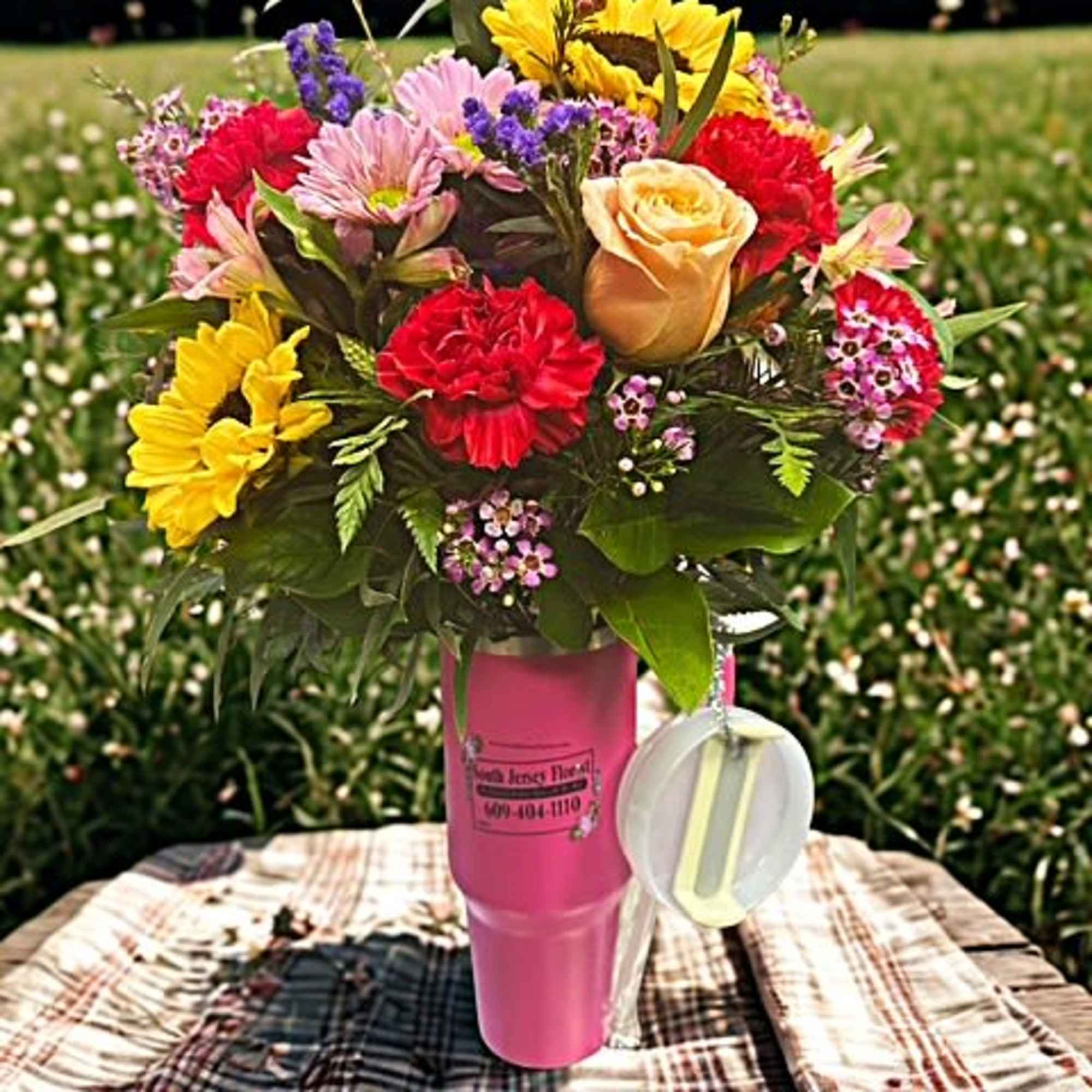 Mixed bouquet in a pink cup-style vase with a hanging tag