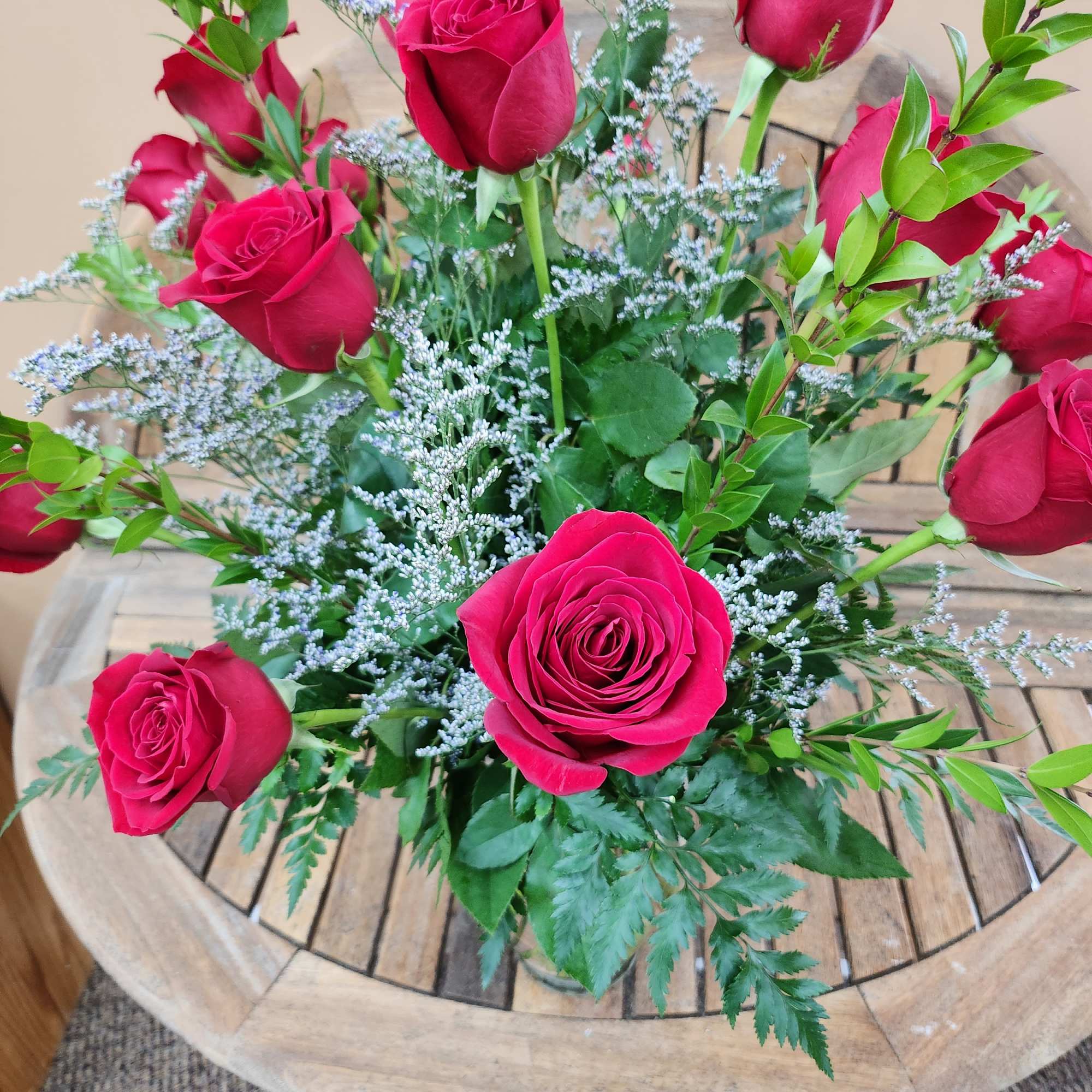 Arrangement of red roses with small white filler flowers on a wooden round table
