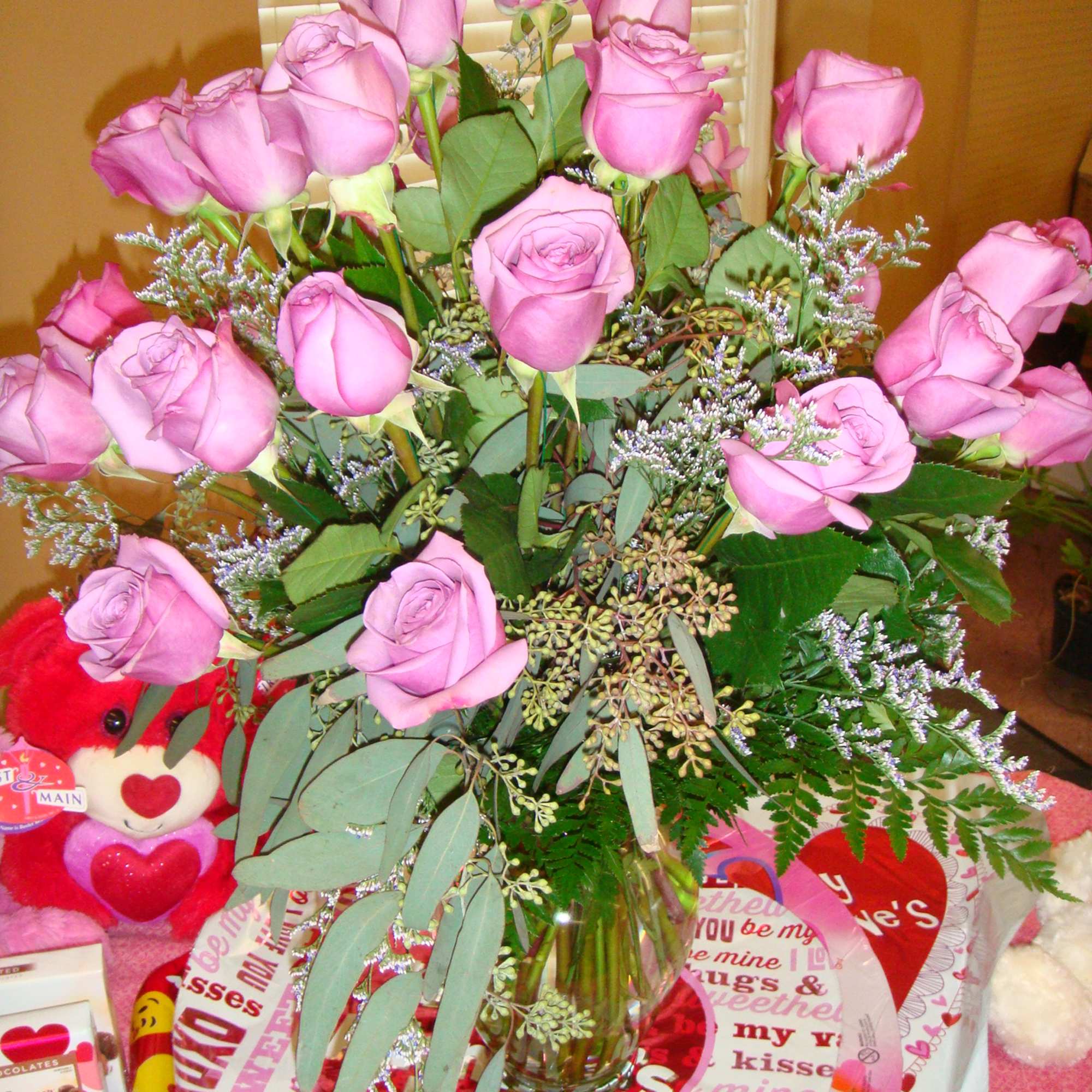 Pink roses in a glass vase with a teddy bear and Valentine gift wrap