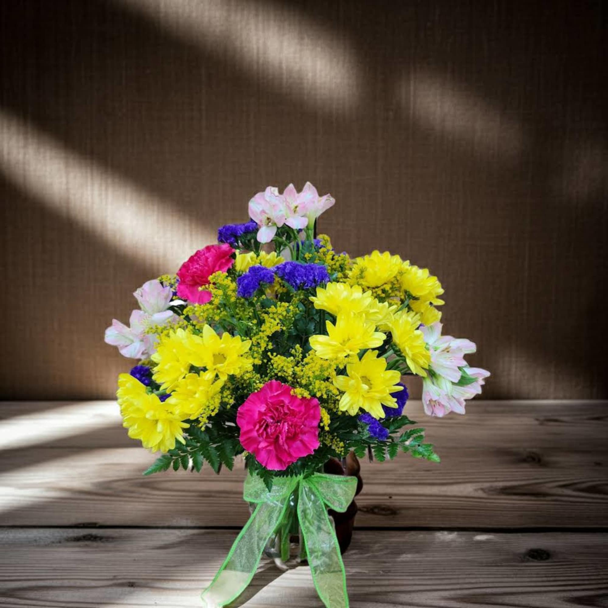 Bright mixed bouquet in a glass vase with a green ribbon
