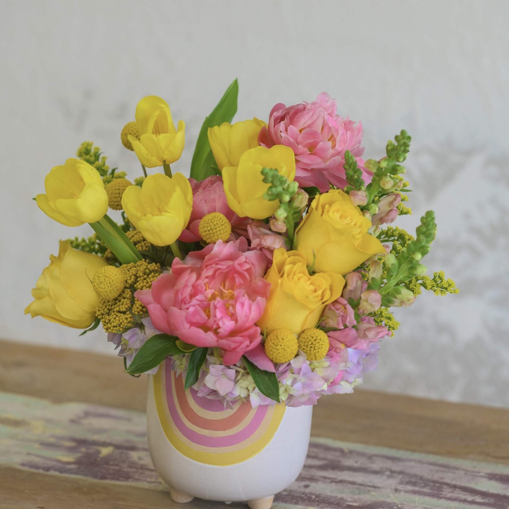 Yellow tulips and pink peonies in a small white vase