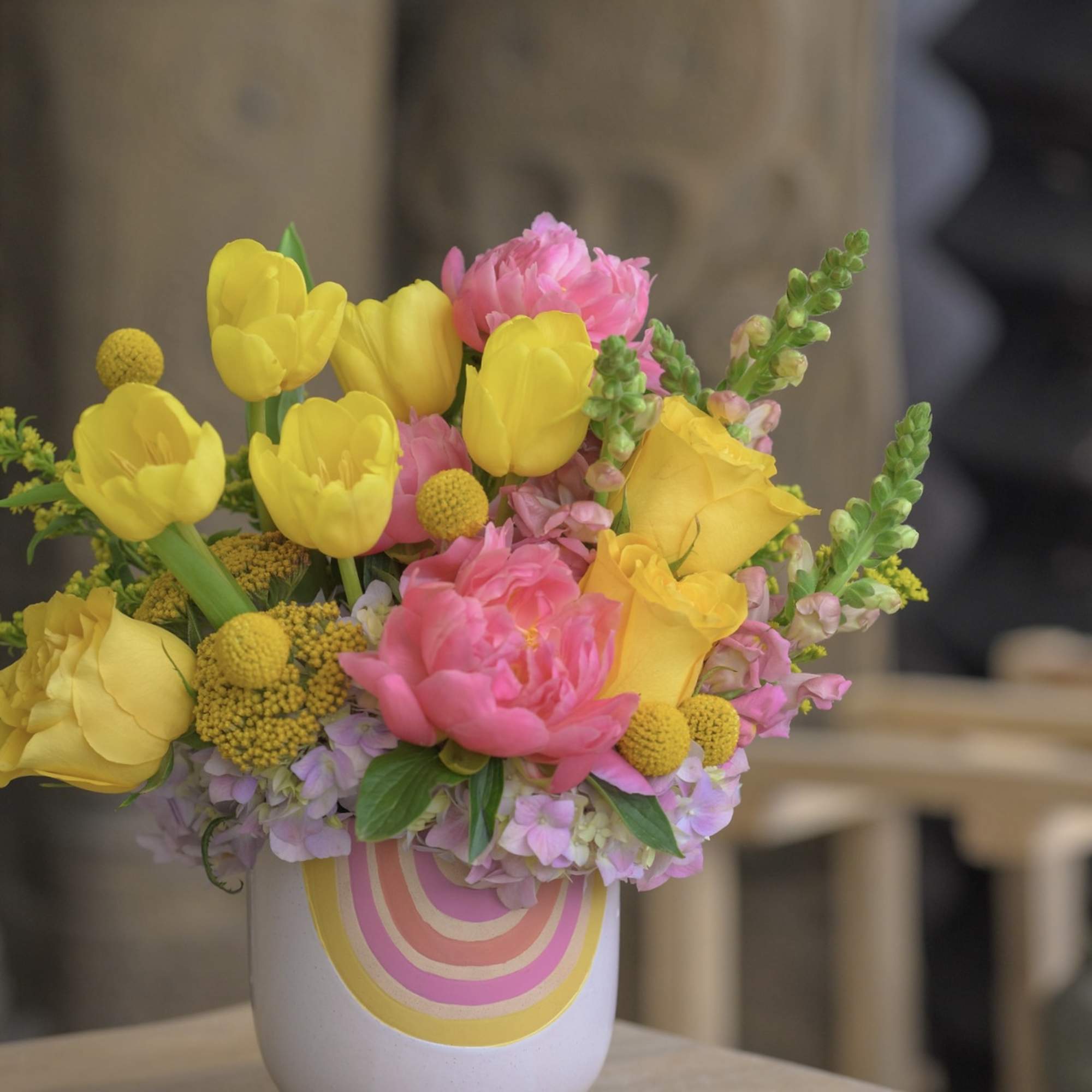 Yellow tulips and pink flowers in a white vase with rainbow stripes