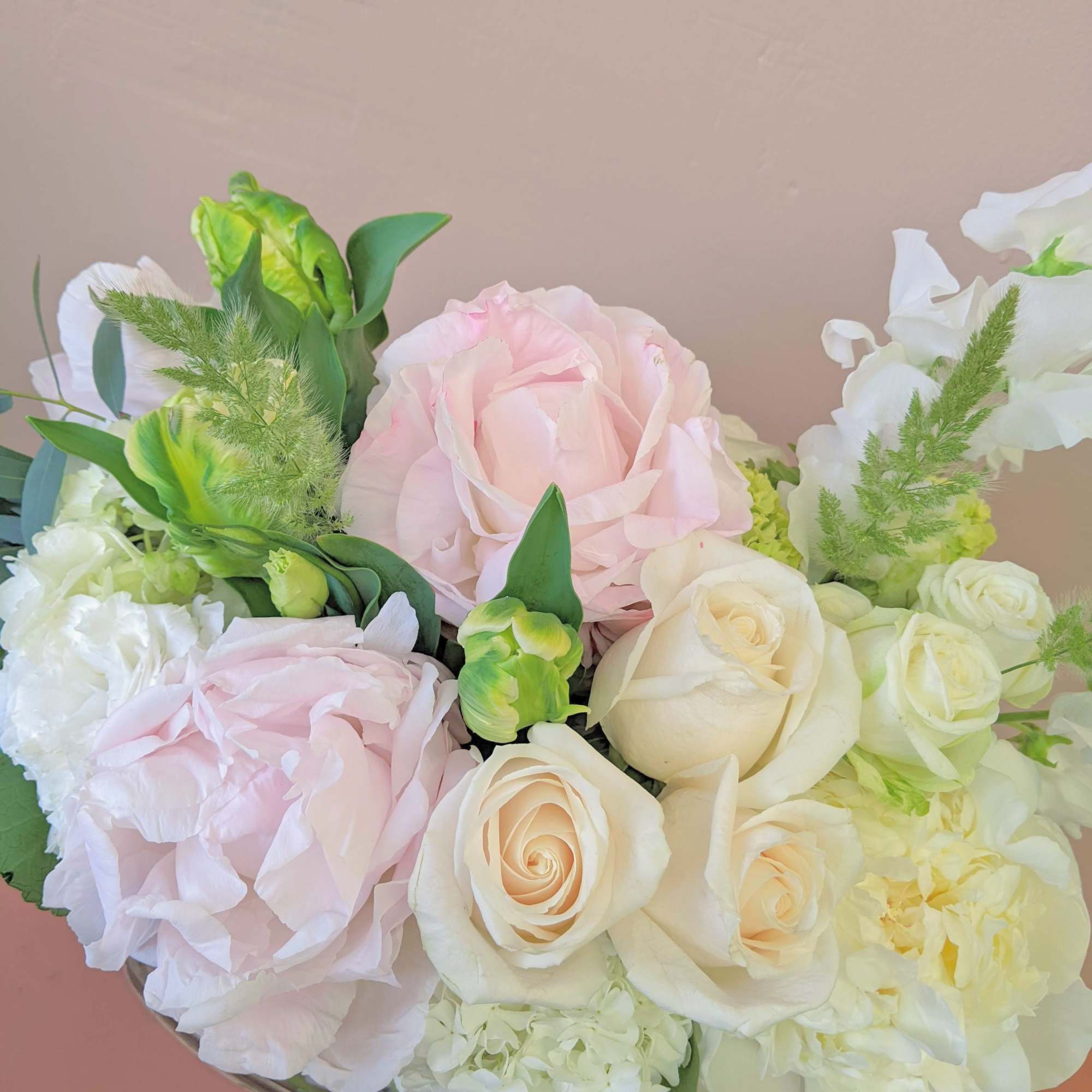 Bouquet of pale pink and white roses with green accents in a low container