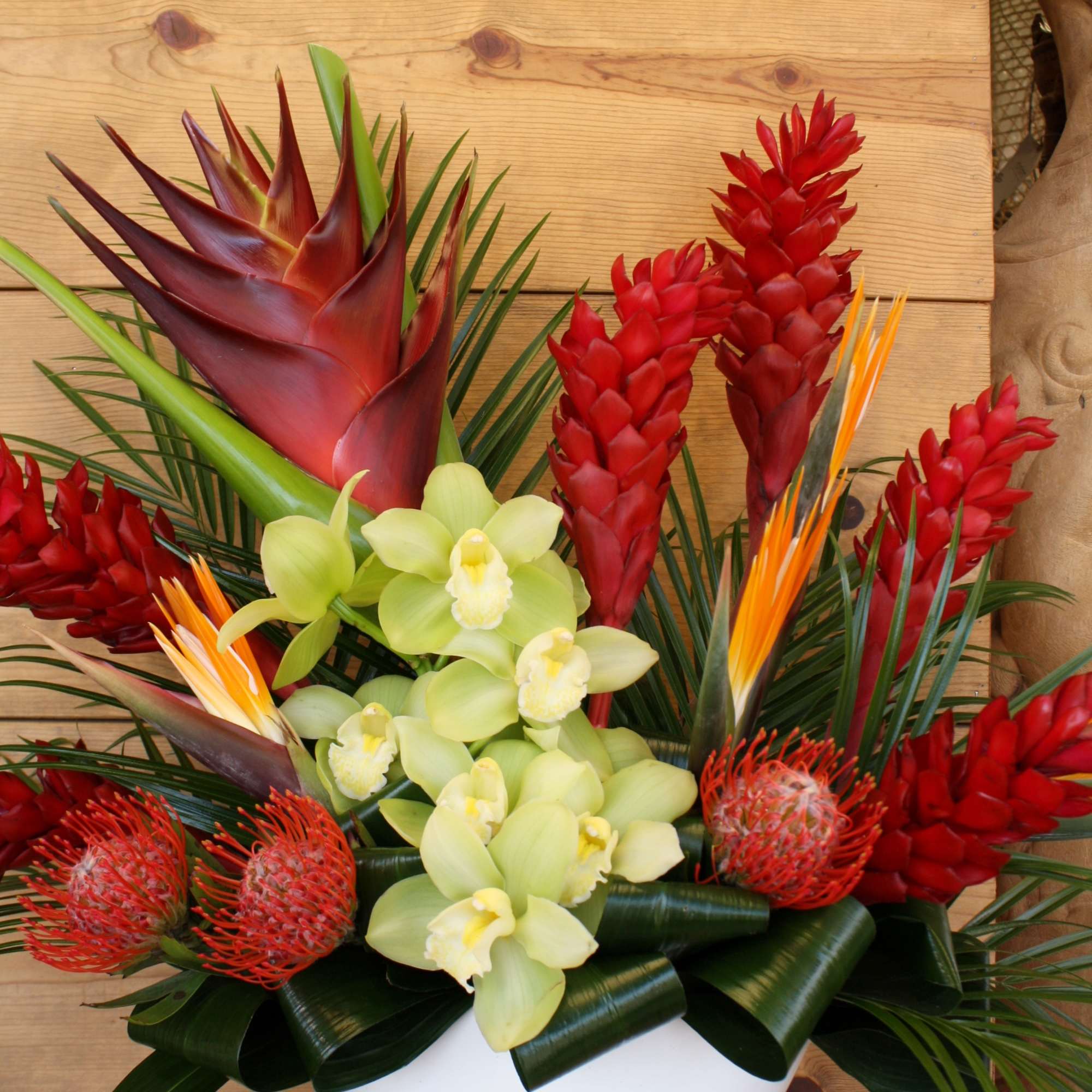 Tropical arrangement with red ginger, orchids, and bird-of-paradise in a white vase