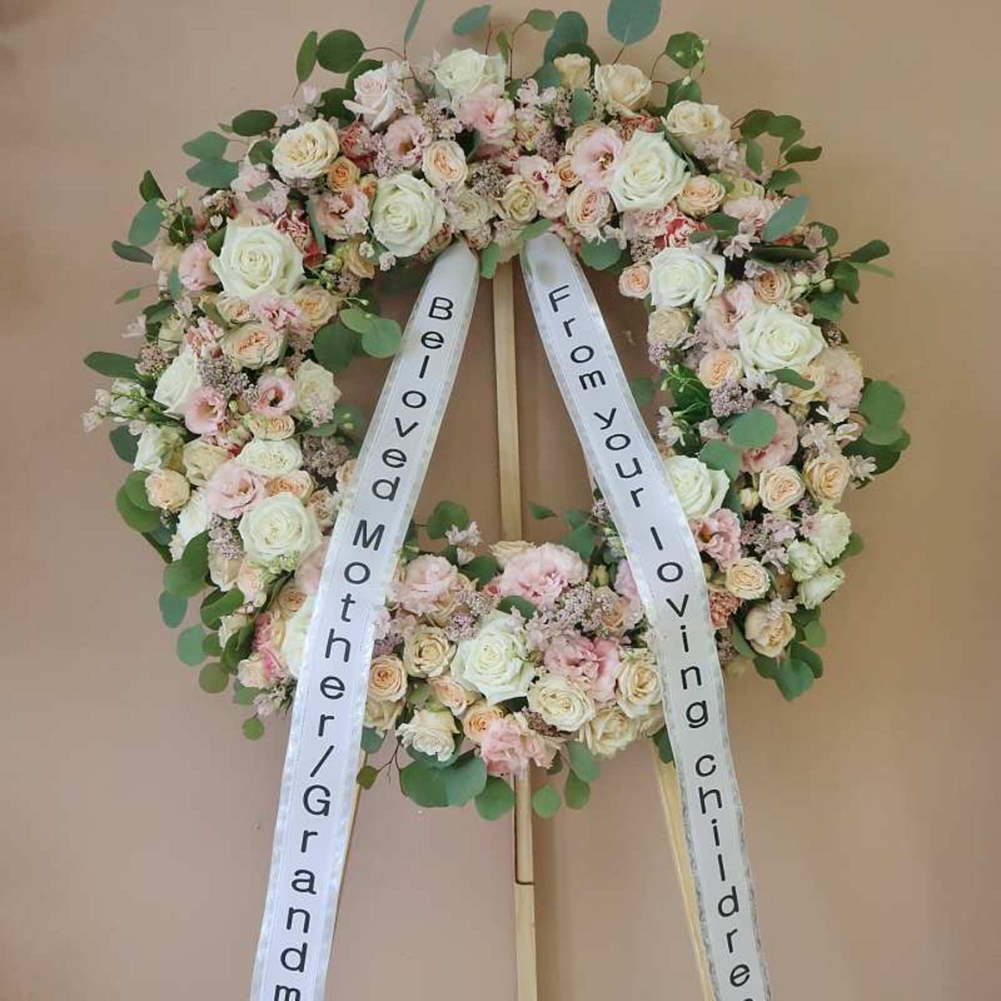 Heart-shaped floral wreath on a stand with white ribbons
