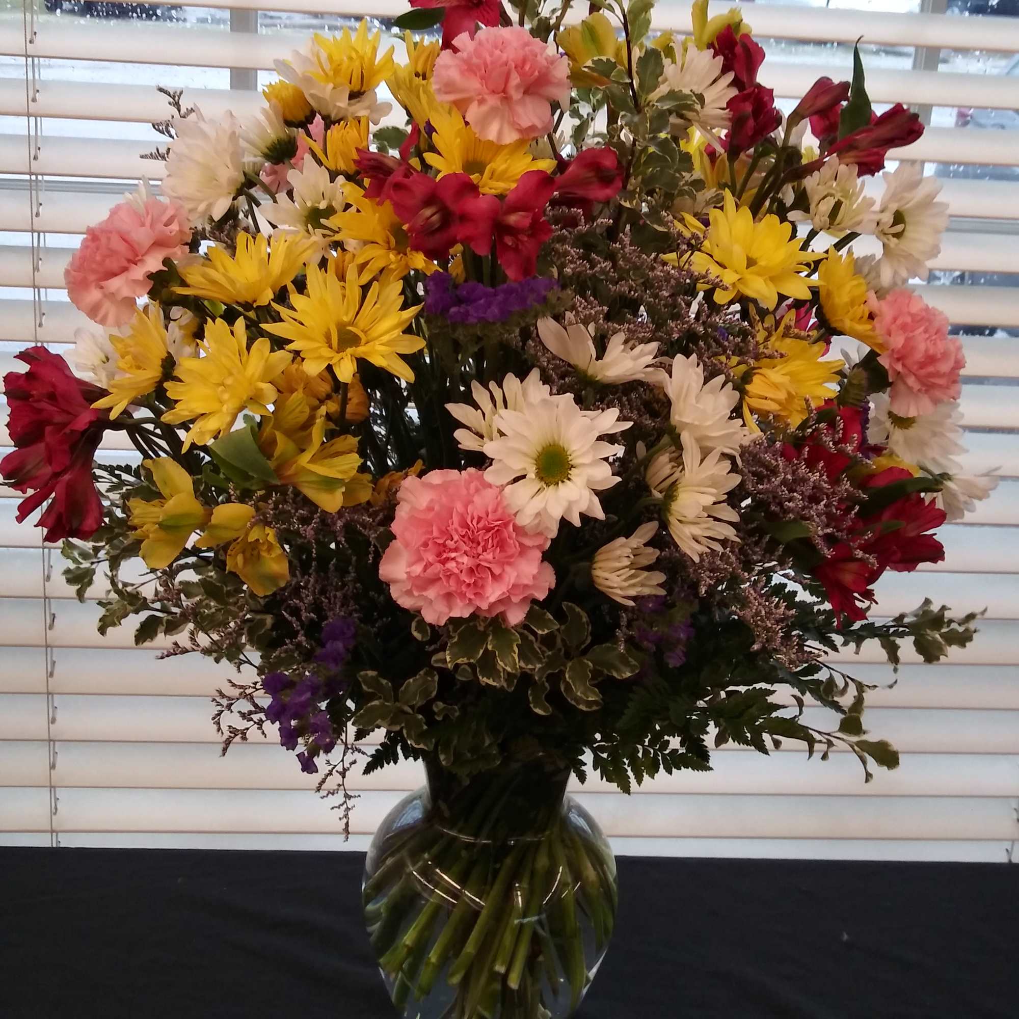Mixed bouquet of yellow, pink, white, and red flowers in a clear glass vase