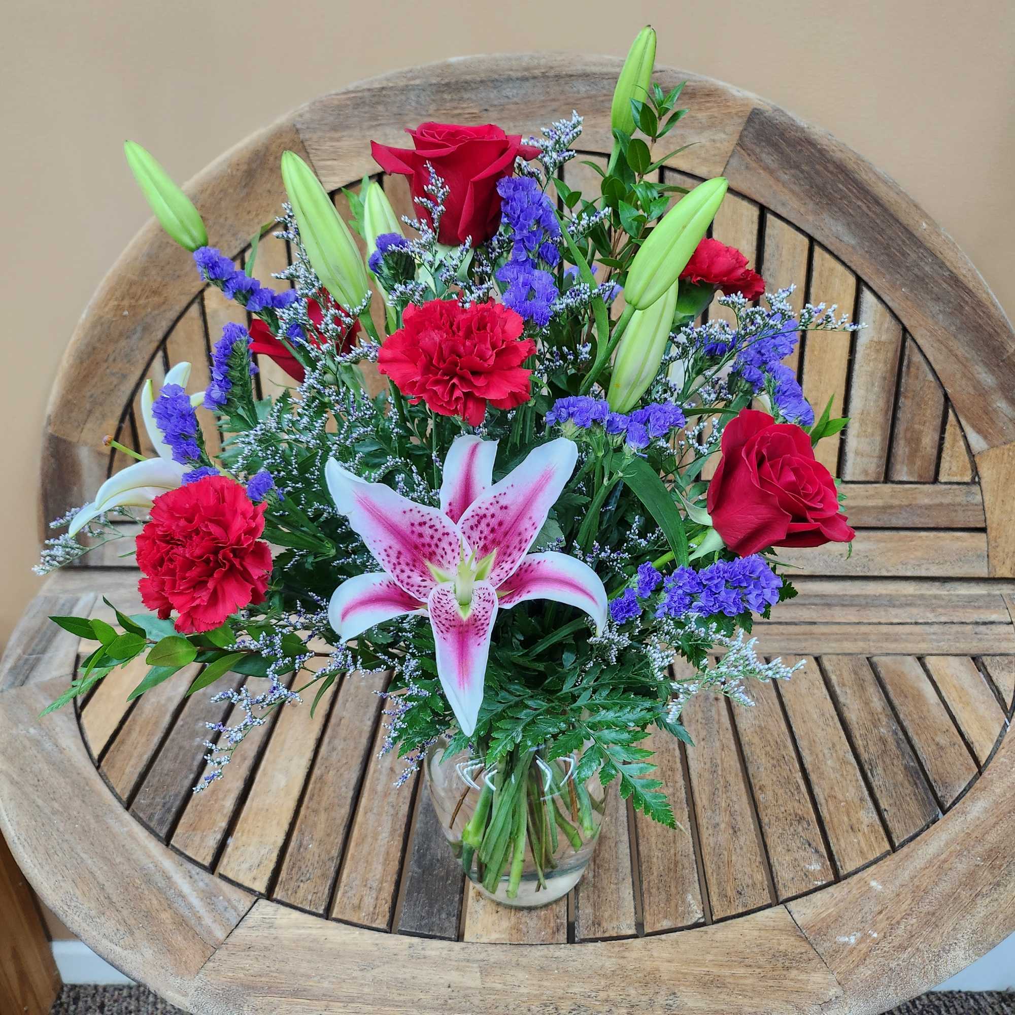 Mixed bouquet of red roses, red carnations, pink lilies and purple filler in a clear glass vase