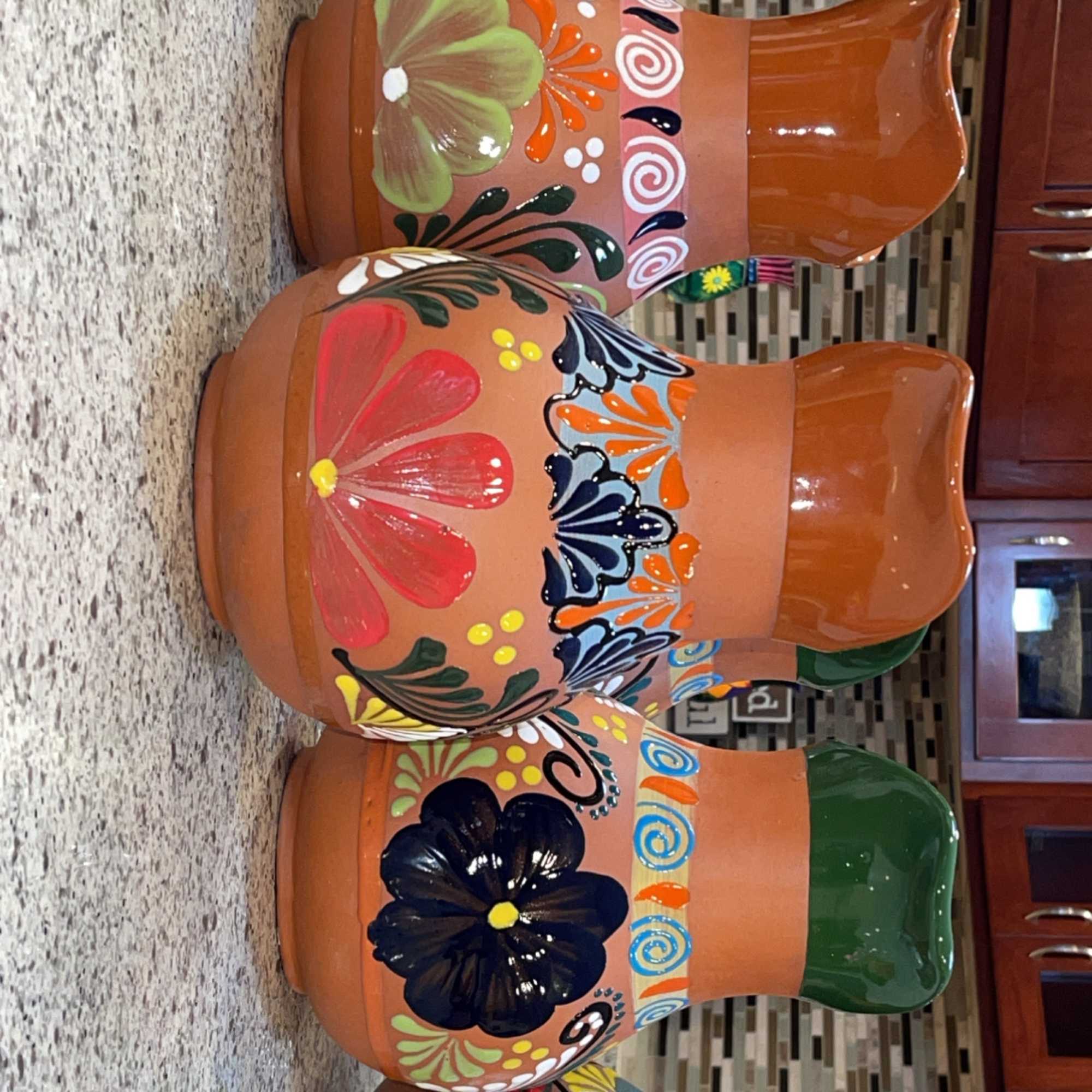 Five painted terracotta planters arranged in a row on a kitchen counter.