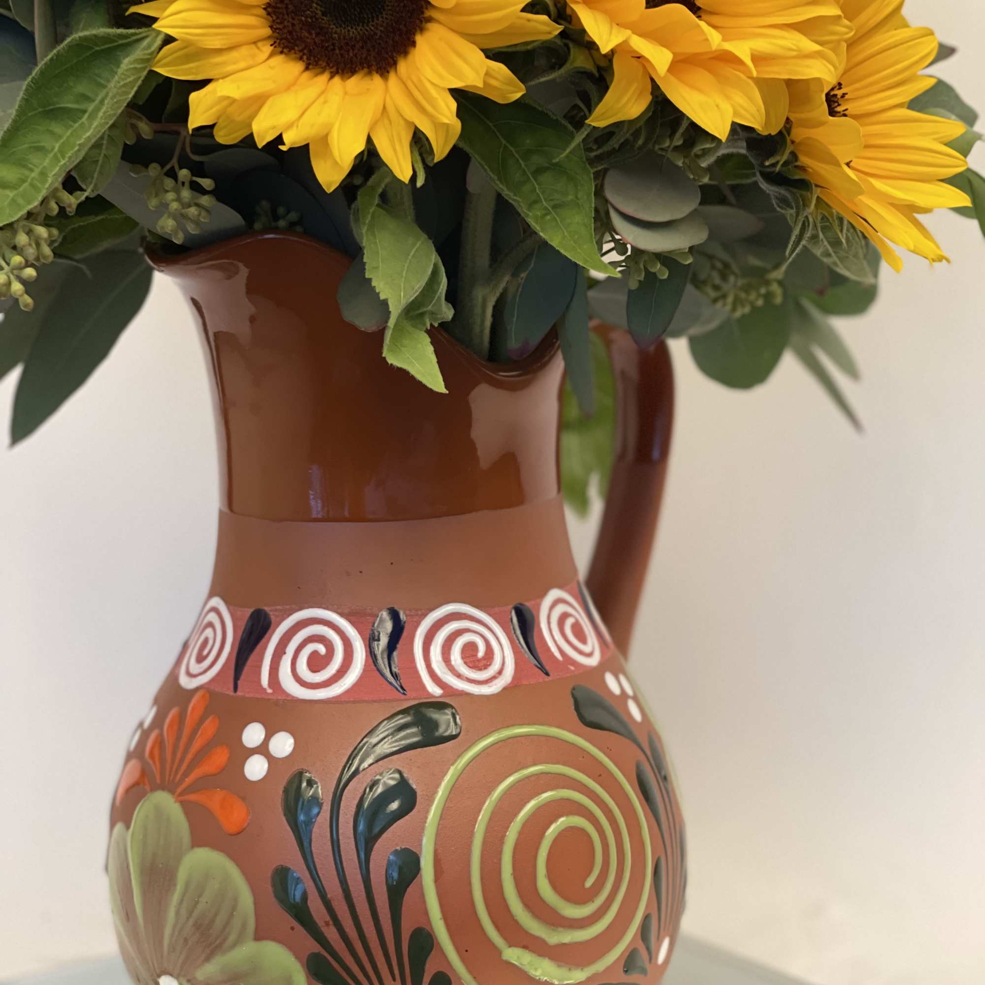 Sunflowers arranged in a painted brown ceramic pitcher