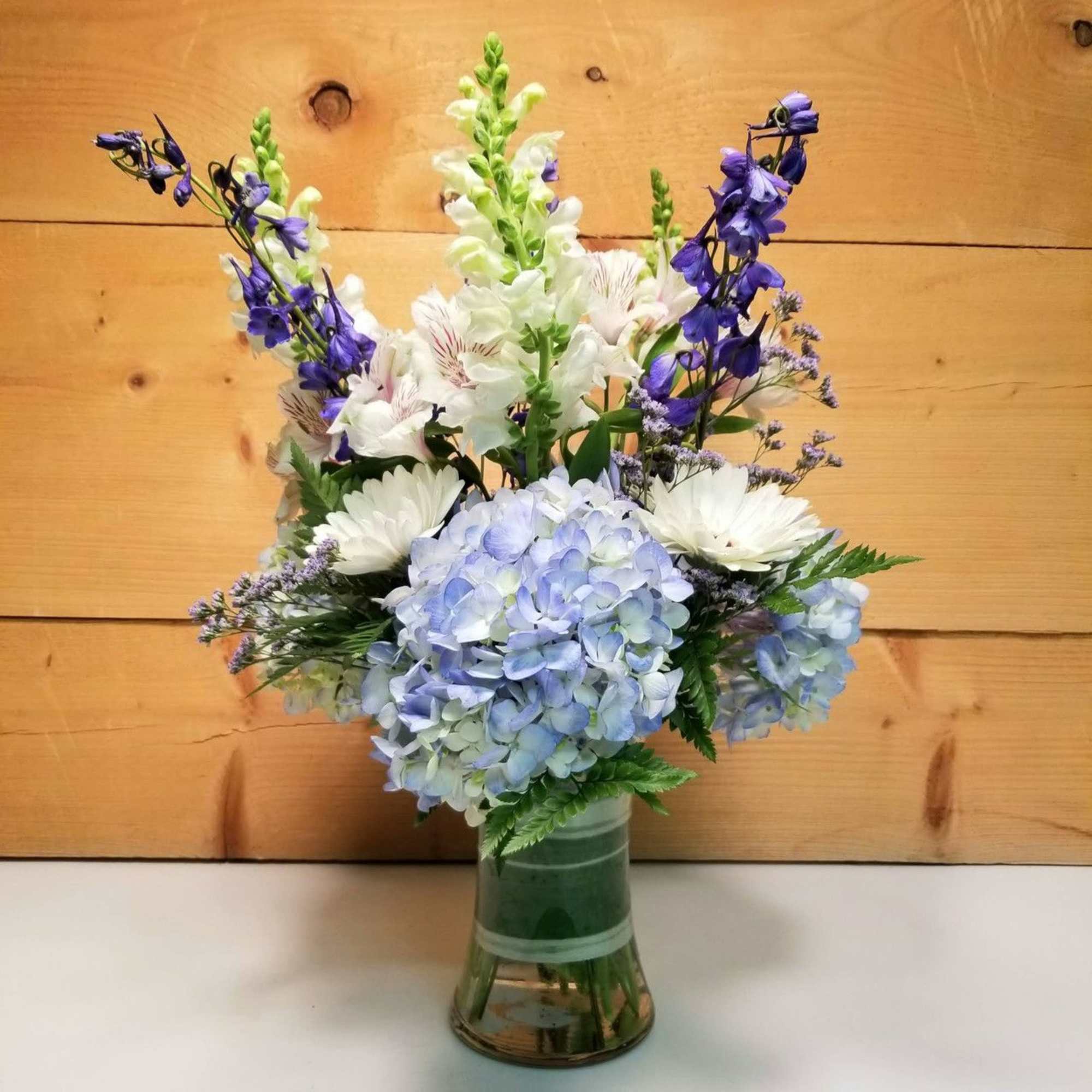 Tall blue and white mixed flower arrangement with purple accents in a clear glass vase