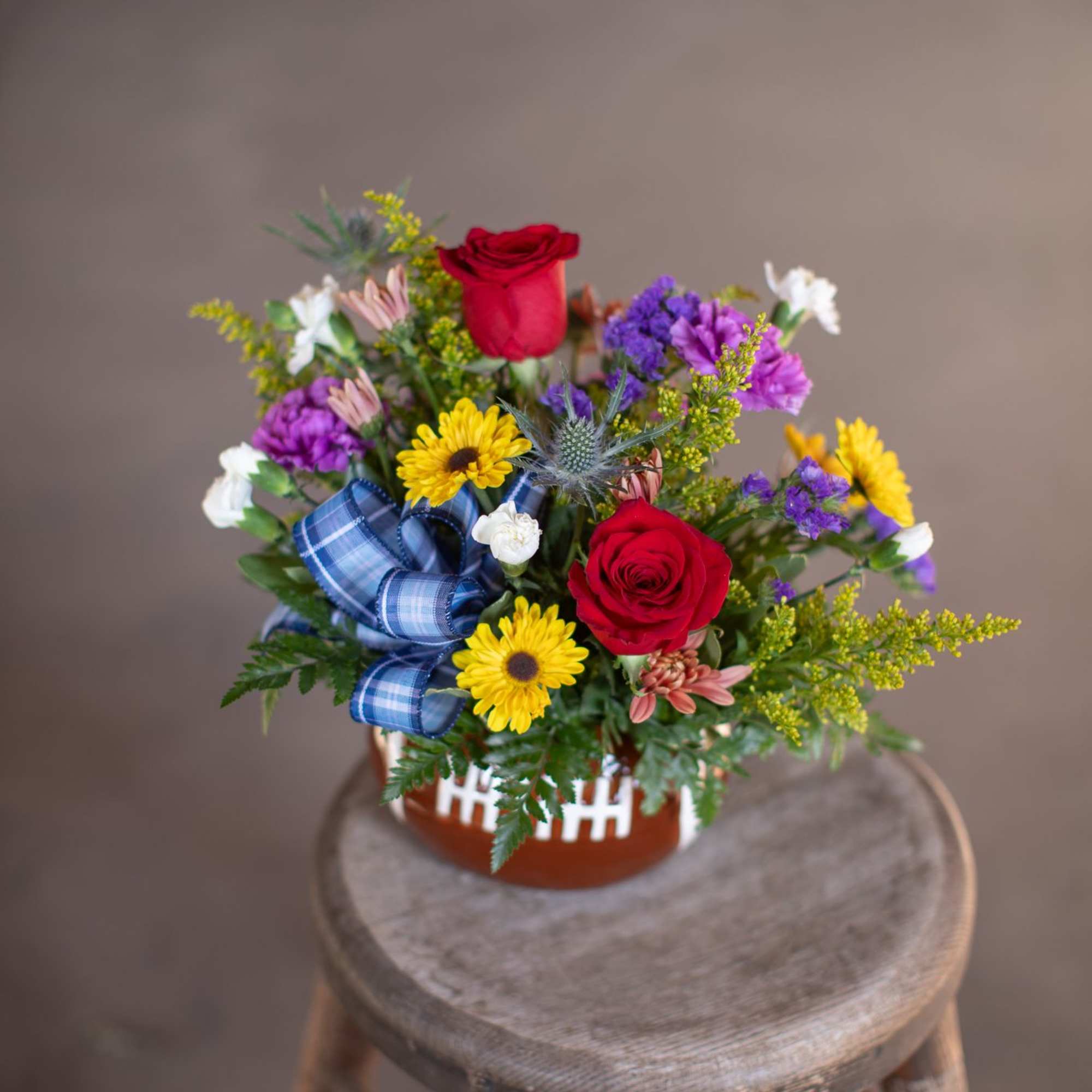 Mixed flower arrangement in a basket with red roses and a blue ribbon