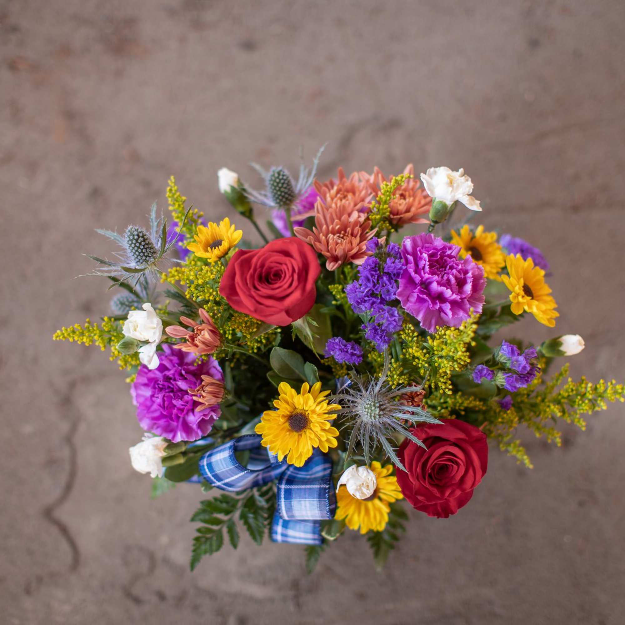 Mixed bouquet with red roses, purple carnations, and yellow daisies tied with a blue ribbon