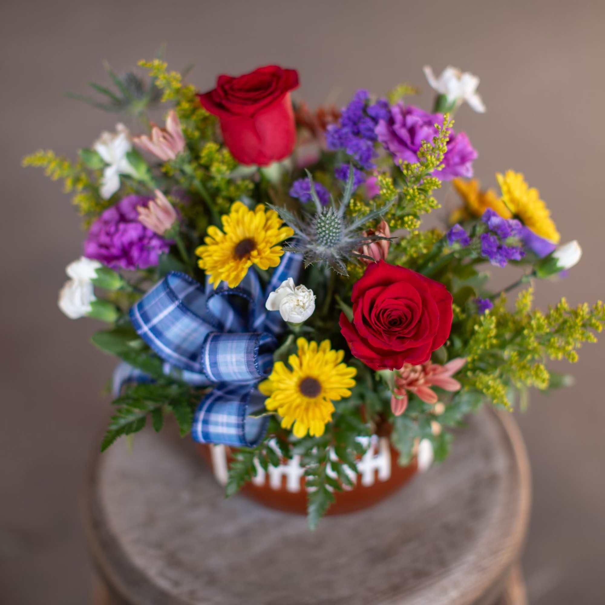 Mixed bouquet with red roses, yellow daisies, and purple flowers in a football-themed container