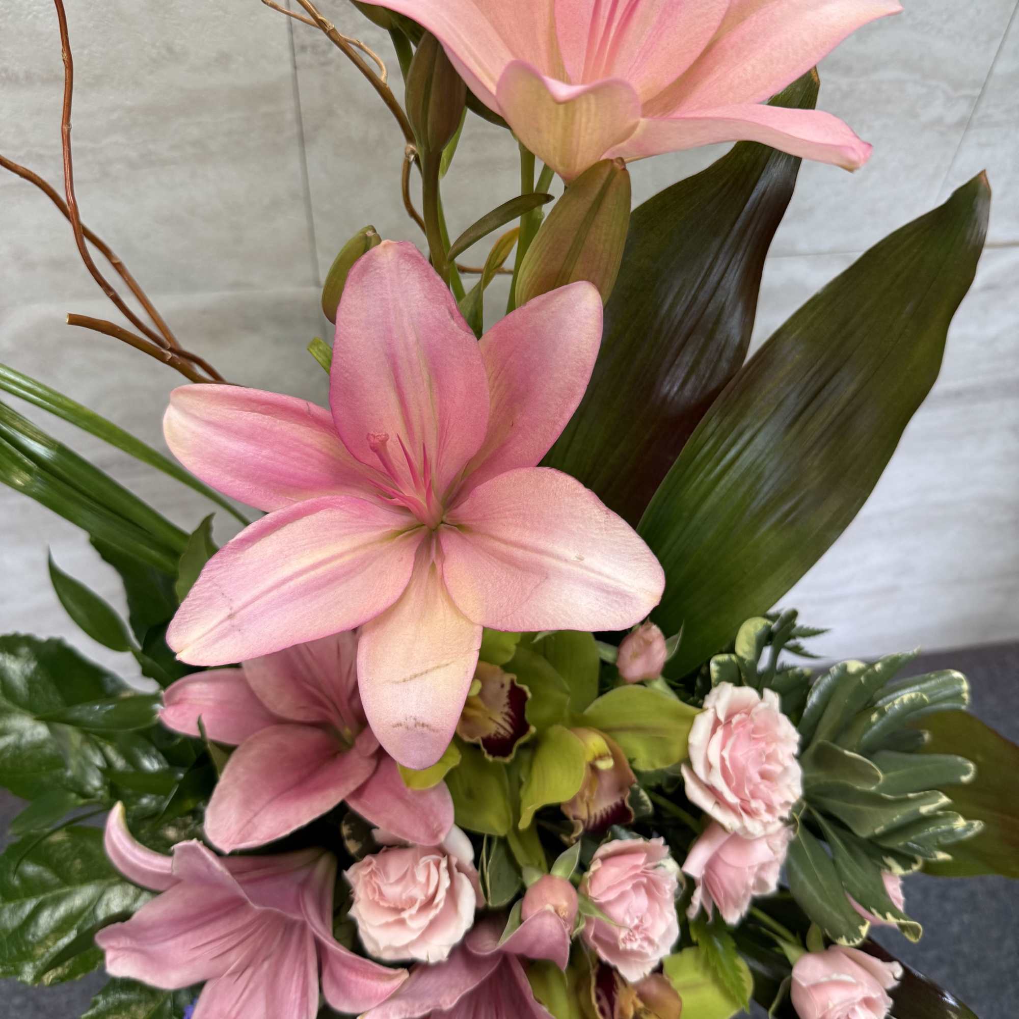 Pink lilies and small pink flowers arranged with broad leaves