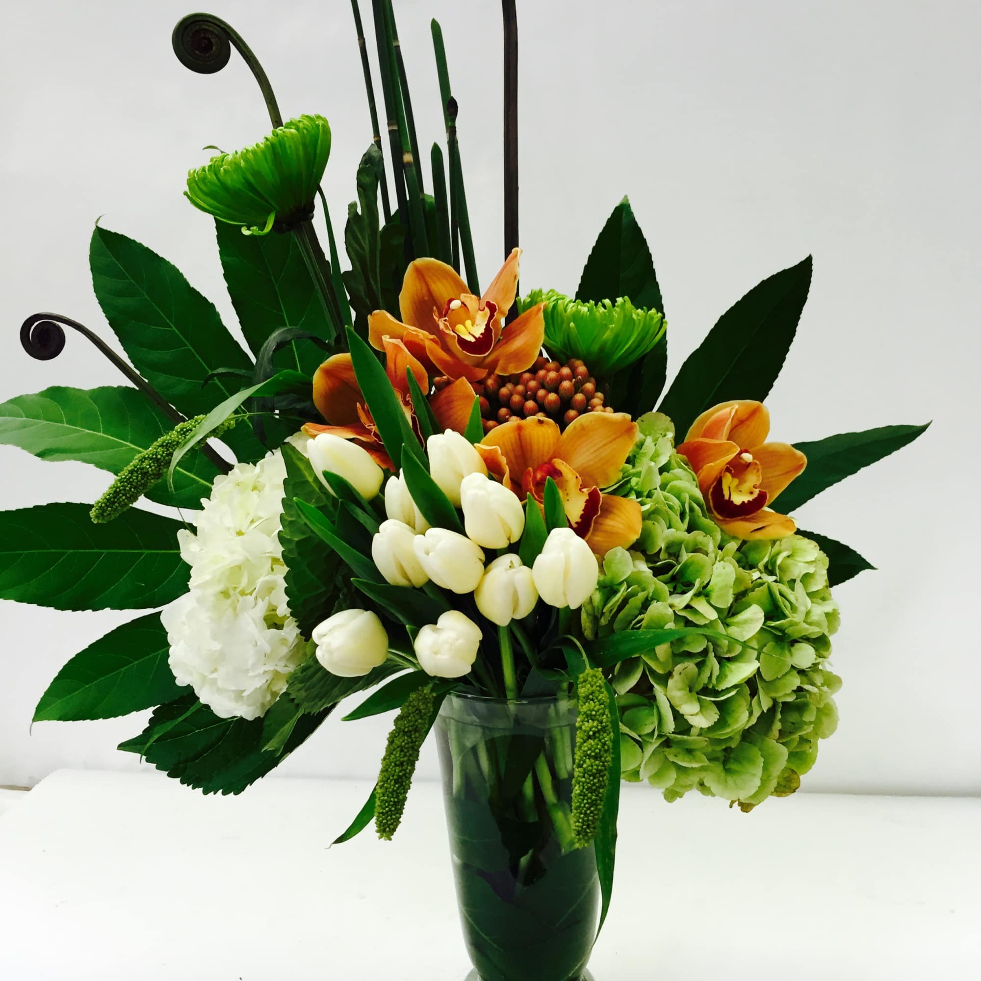 Orange orchids and white tulips in a tall glass vase