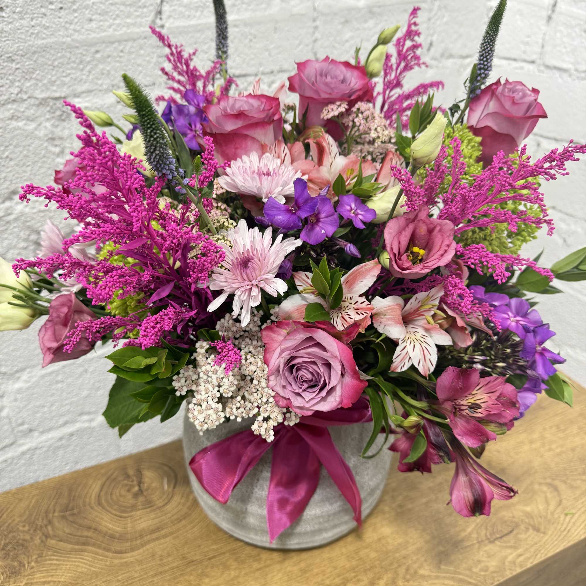 Pink and purple mixed bouquet in a gray vase with a satin ribbon