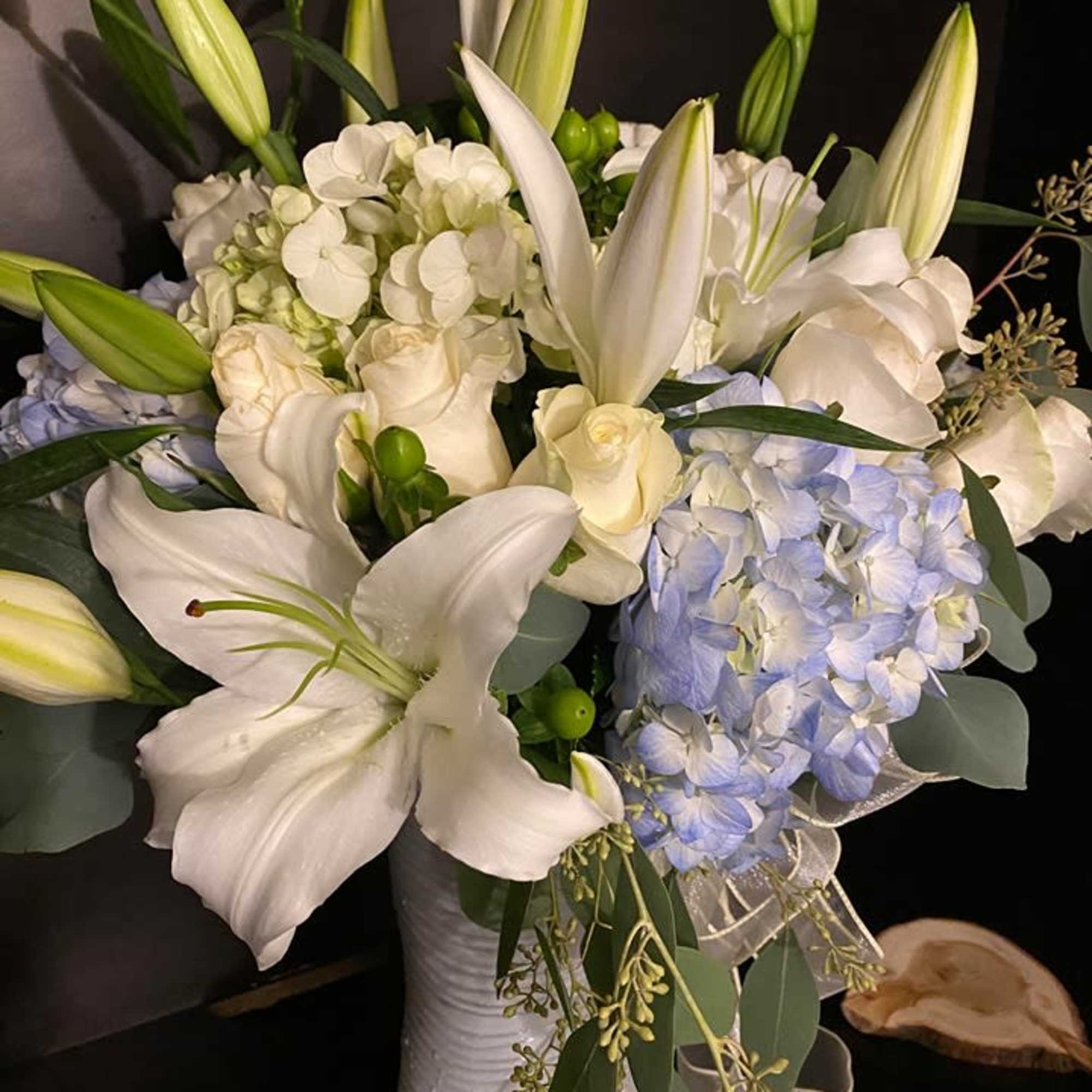 White lilies and pale blue hydrangeas in a tall white vase