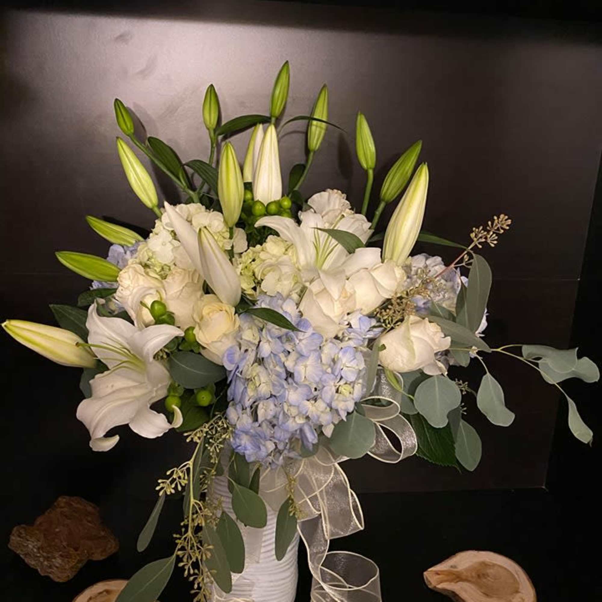White lilies and pale blue hydrangeas in a white vase with ribbon