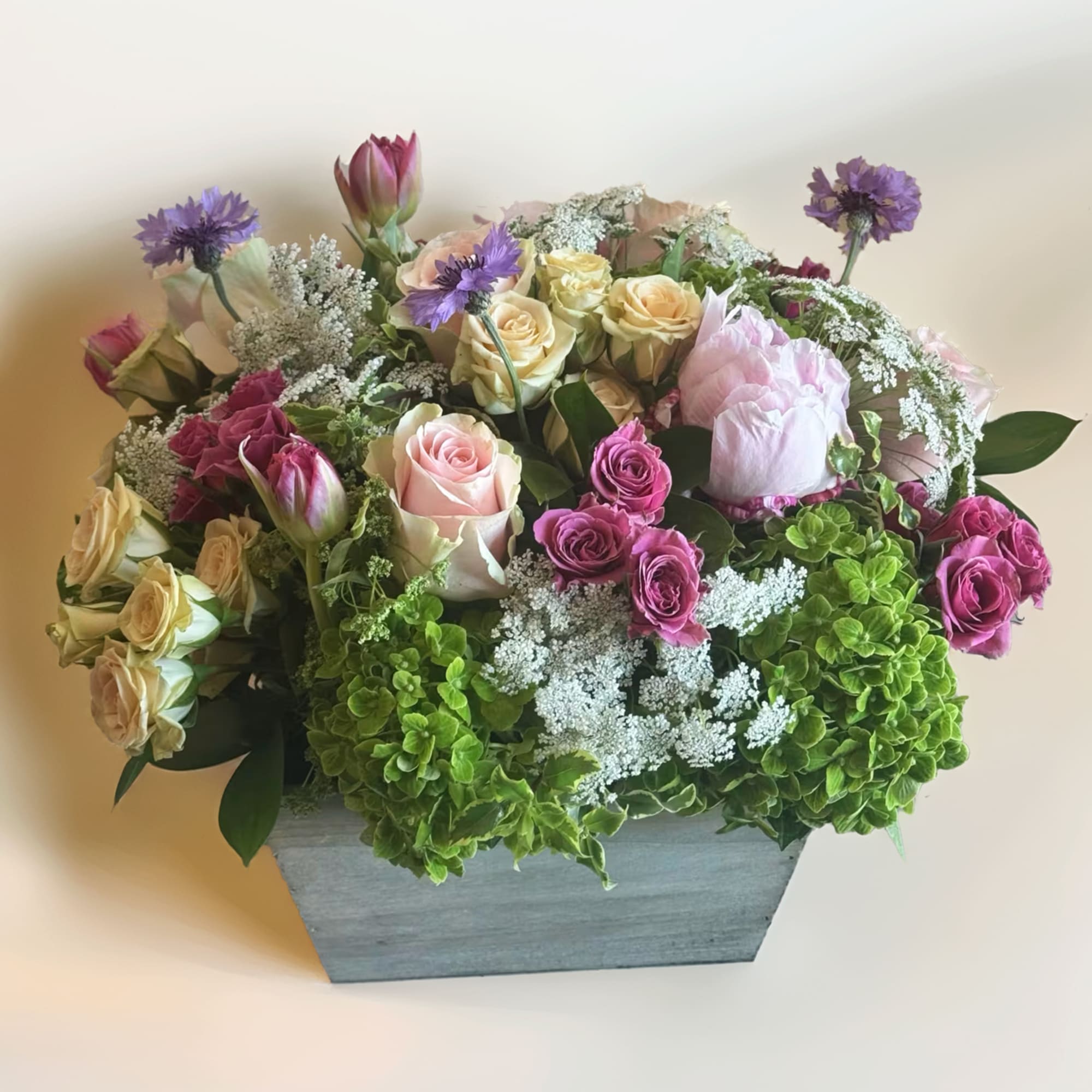 Mixed bouquet of roses, hydrangeas, and purple flowers in a gray wooden box