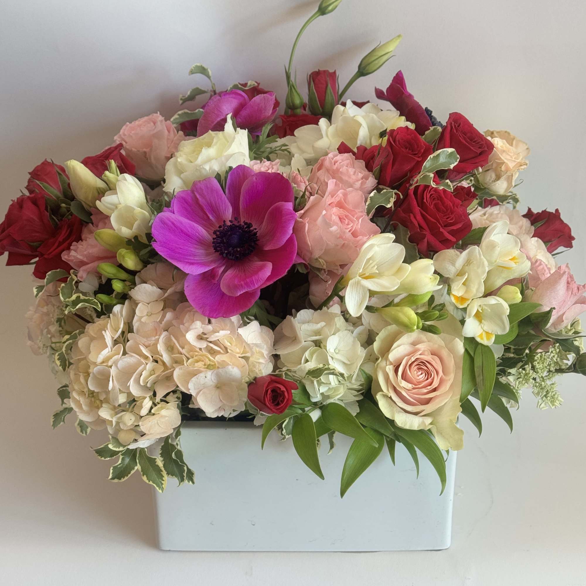 Mixed bouquet in a white rectangular vase with pink, red, and white blooms