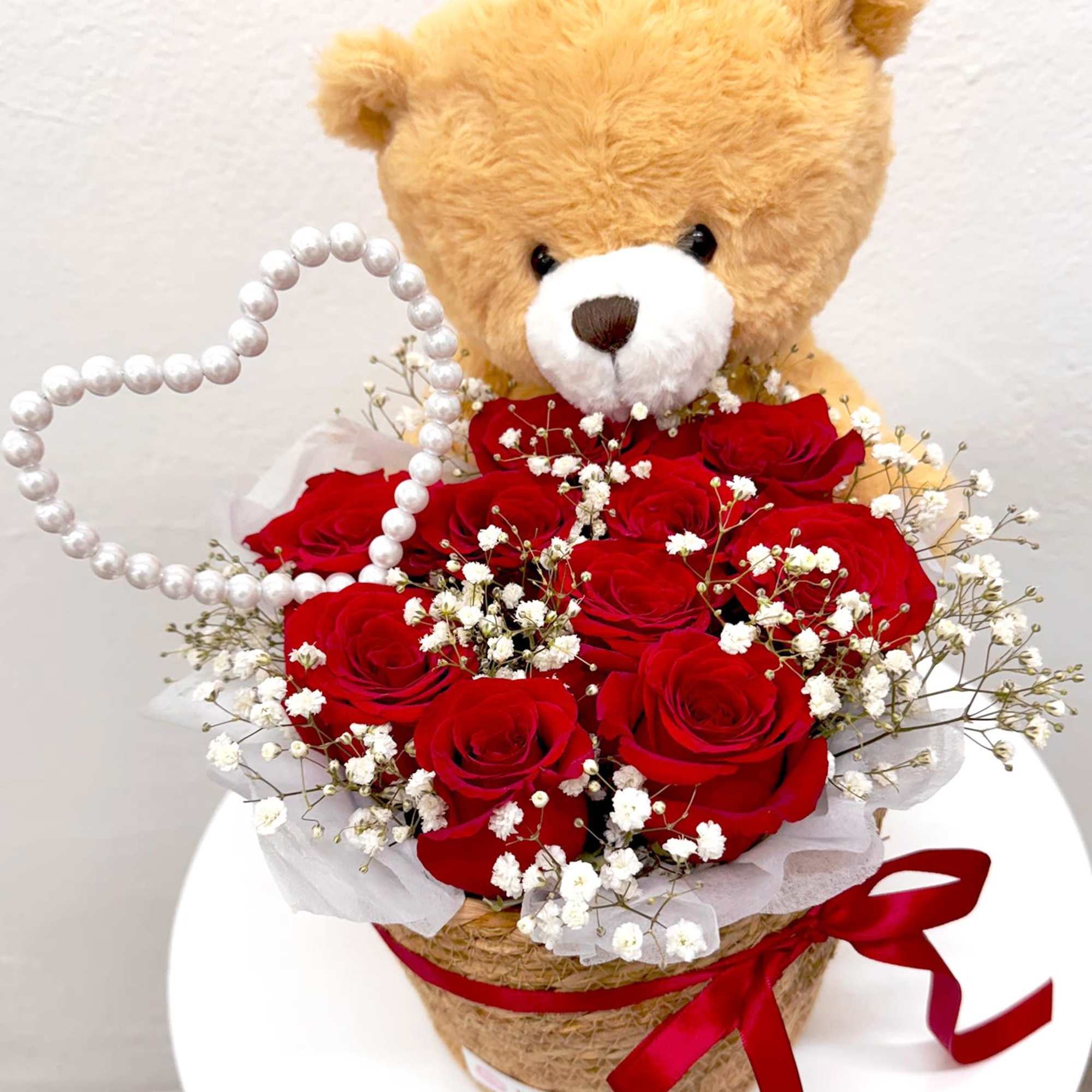 Teddy bear above a bouquet of red roses in a wrapped basket