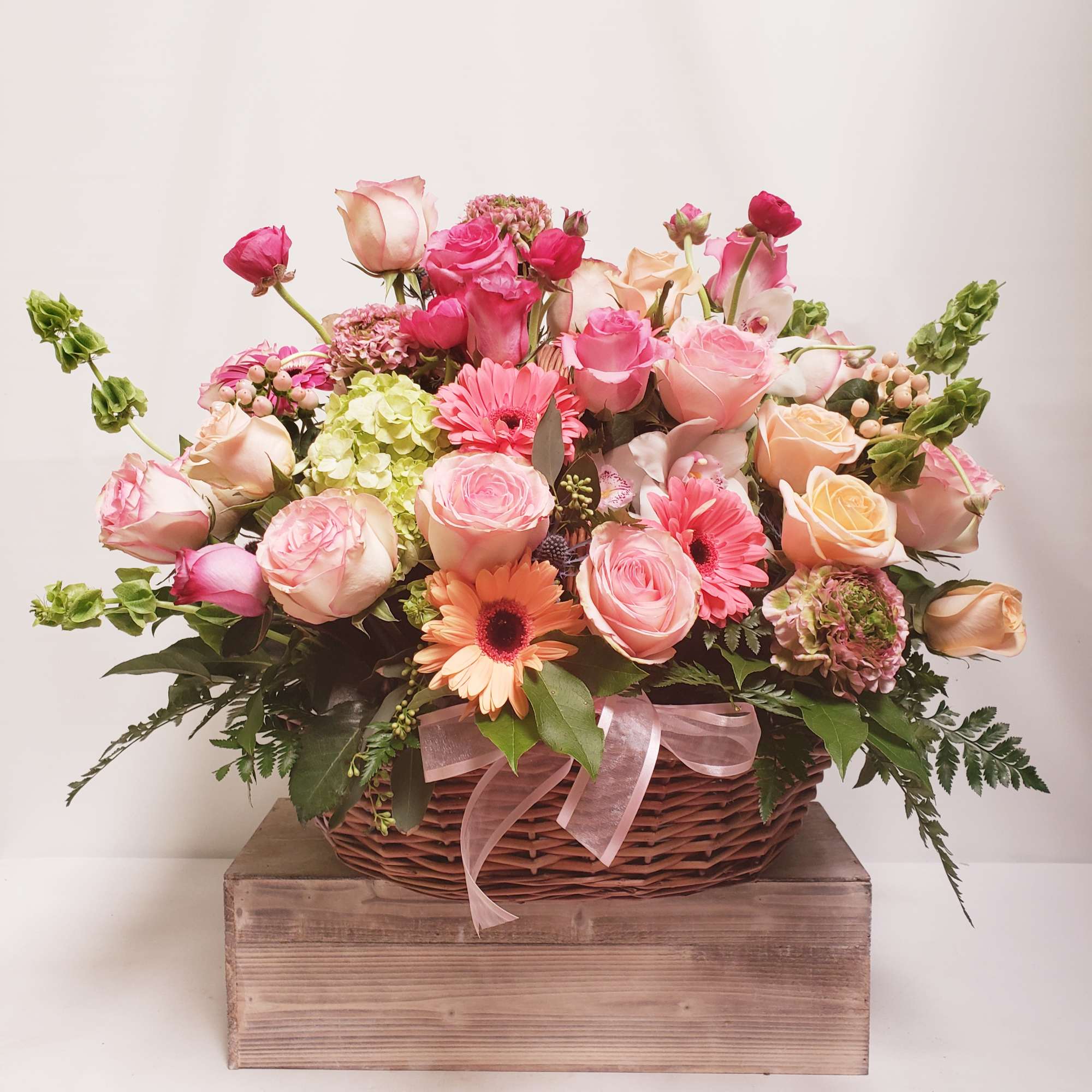 Pink and peach flower arrangement in a wicker basket with a ribbon