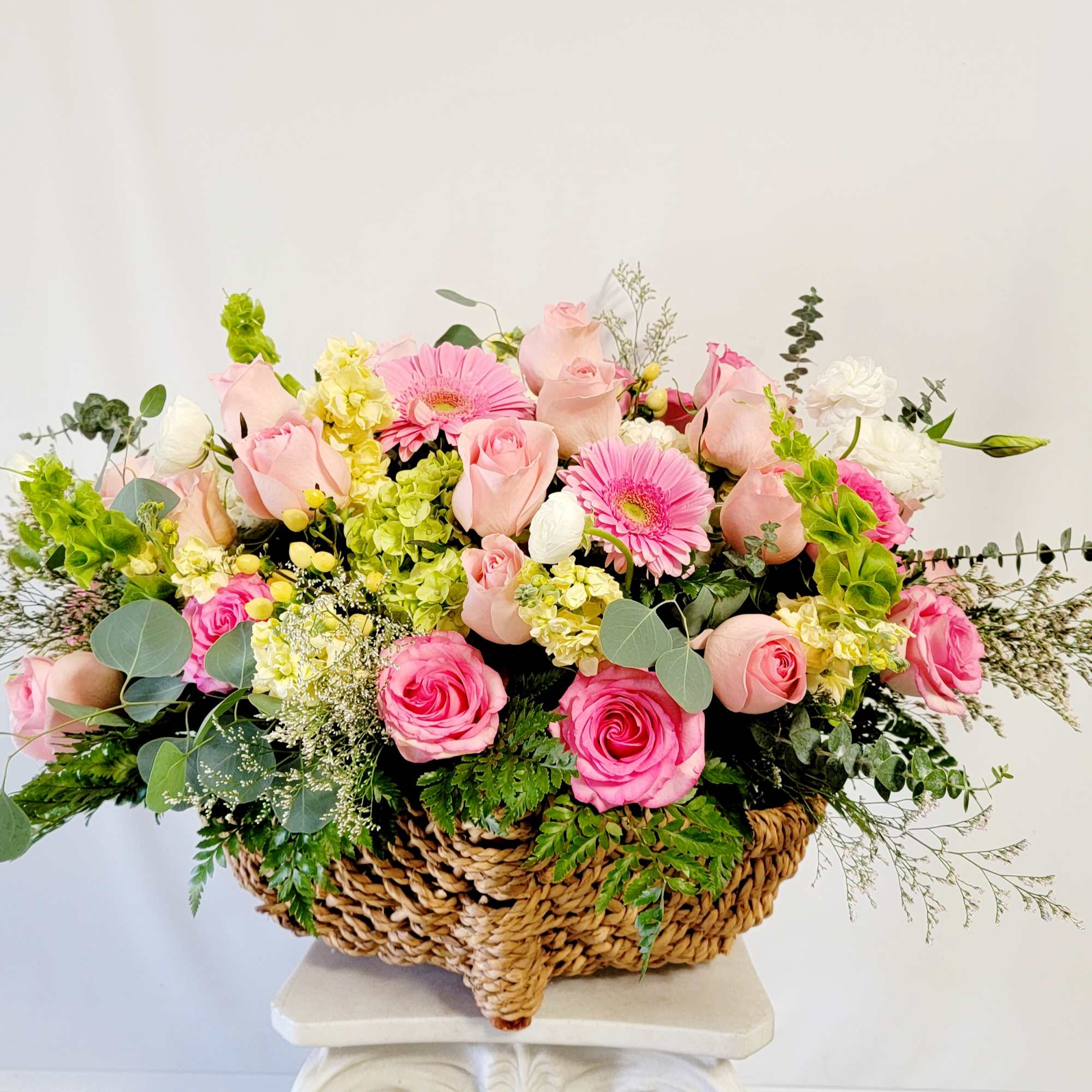 Basket arrangement of pink roses, pink gerbera daisies, and white blooms