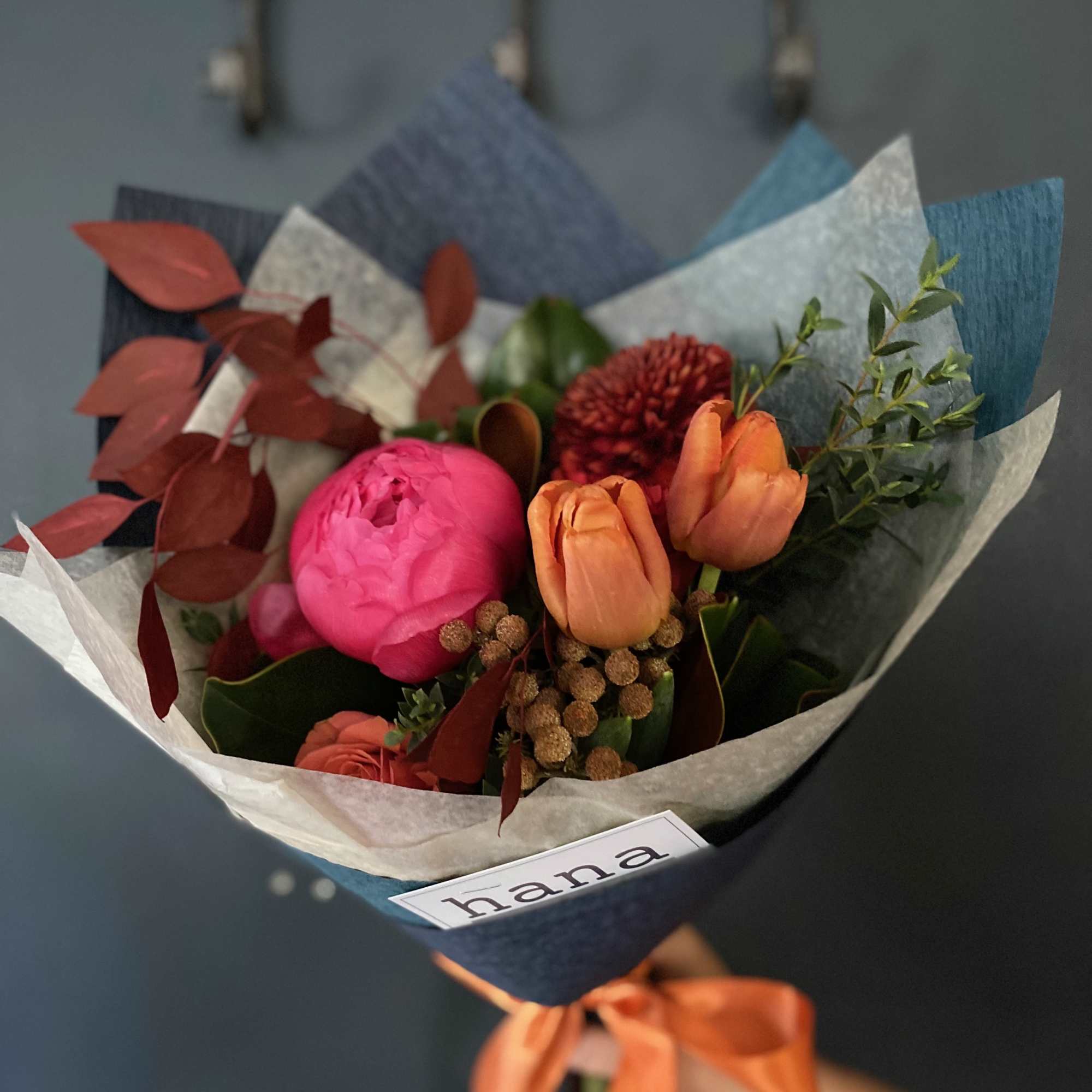 Hand-tied bouquet with pink peonies and orange tulips wrapped in blue paper