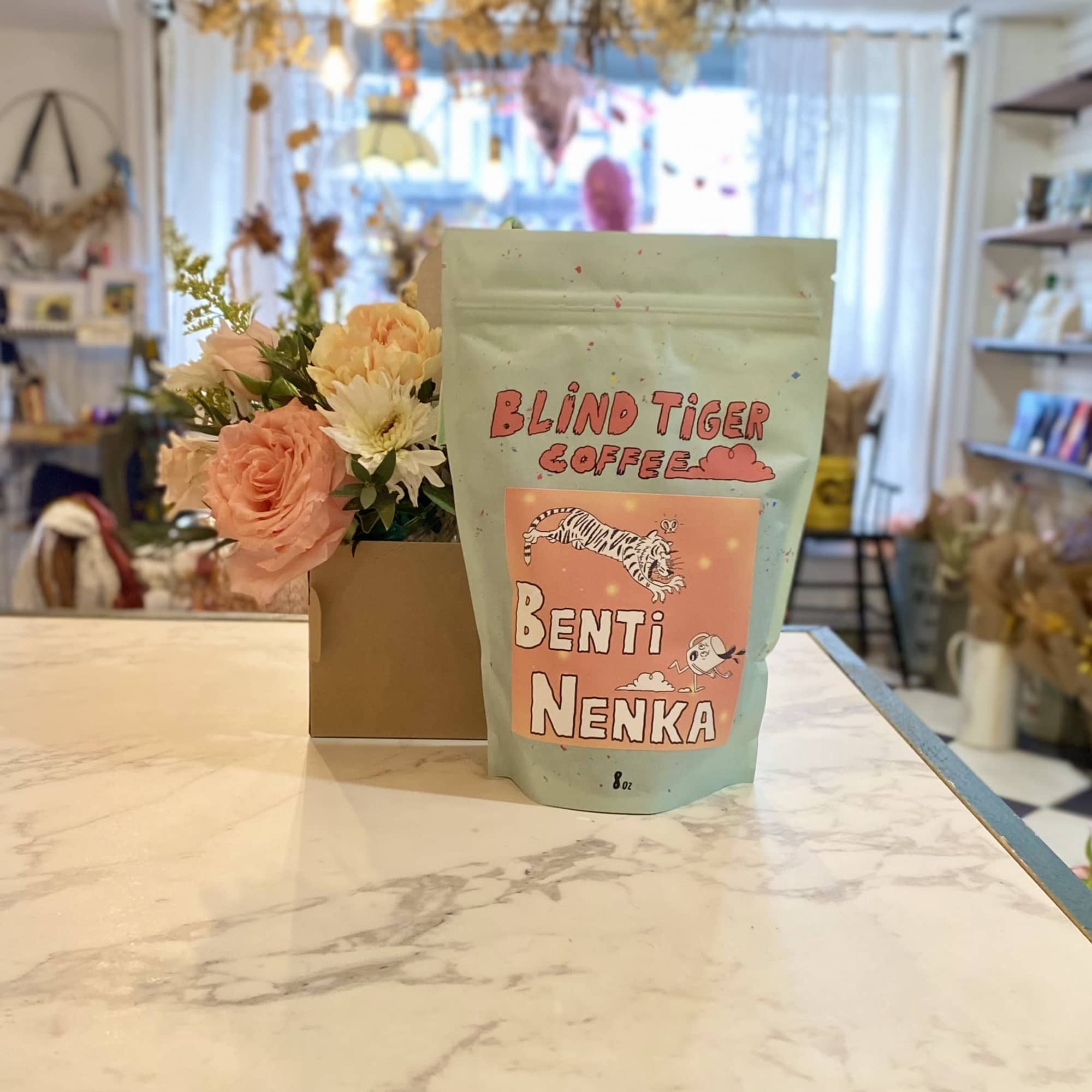 Small flower arrangement beside a mint coffee bag on a counter