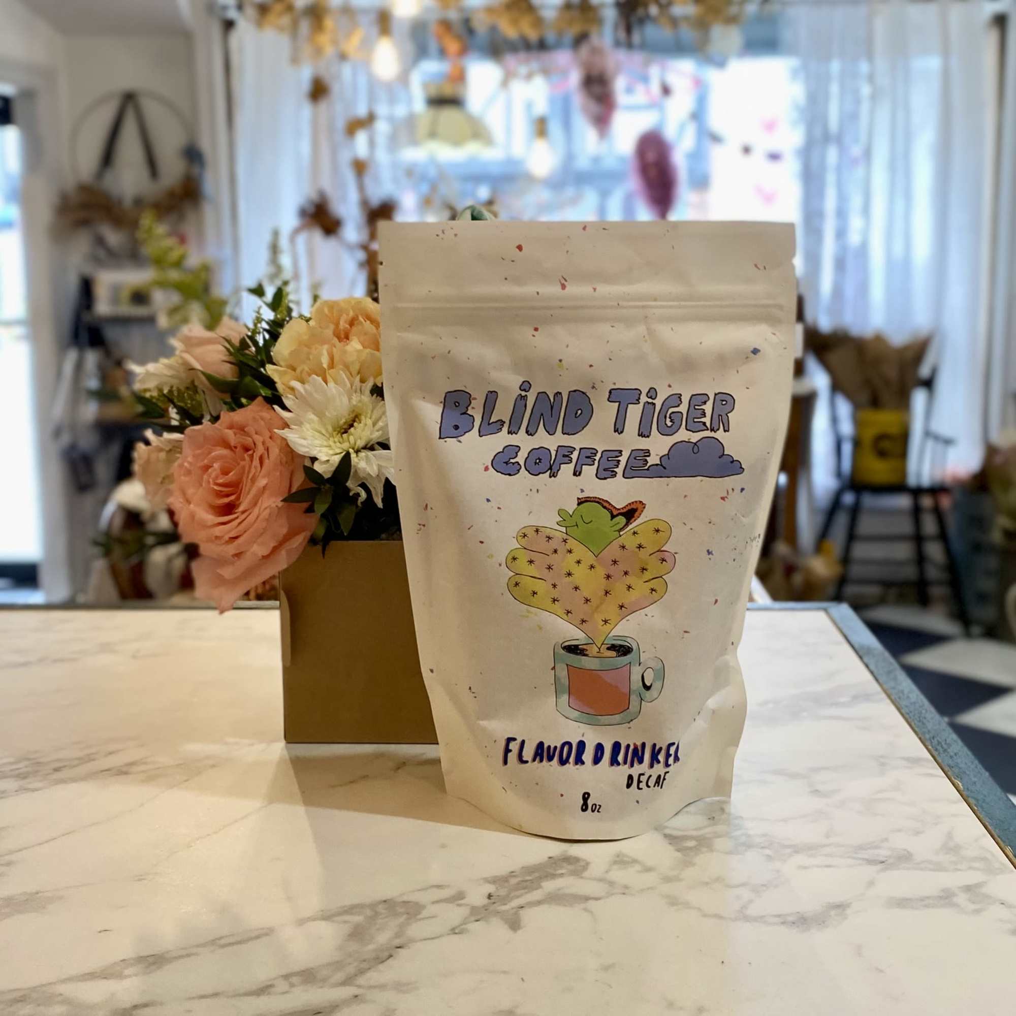 Coffee bag beside a small peach and white flower arrangement