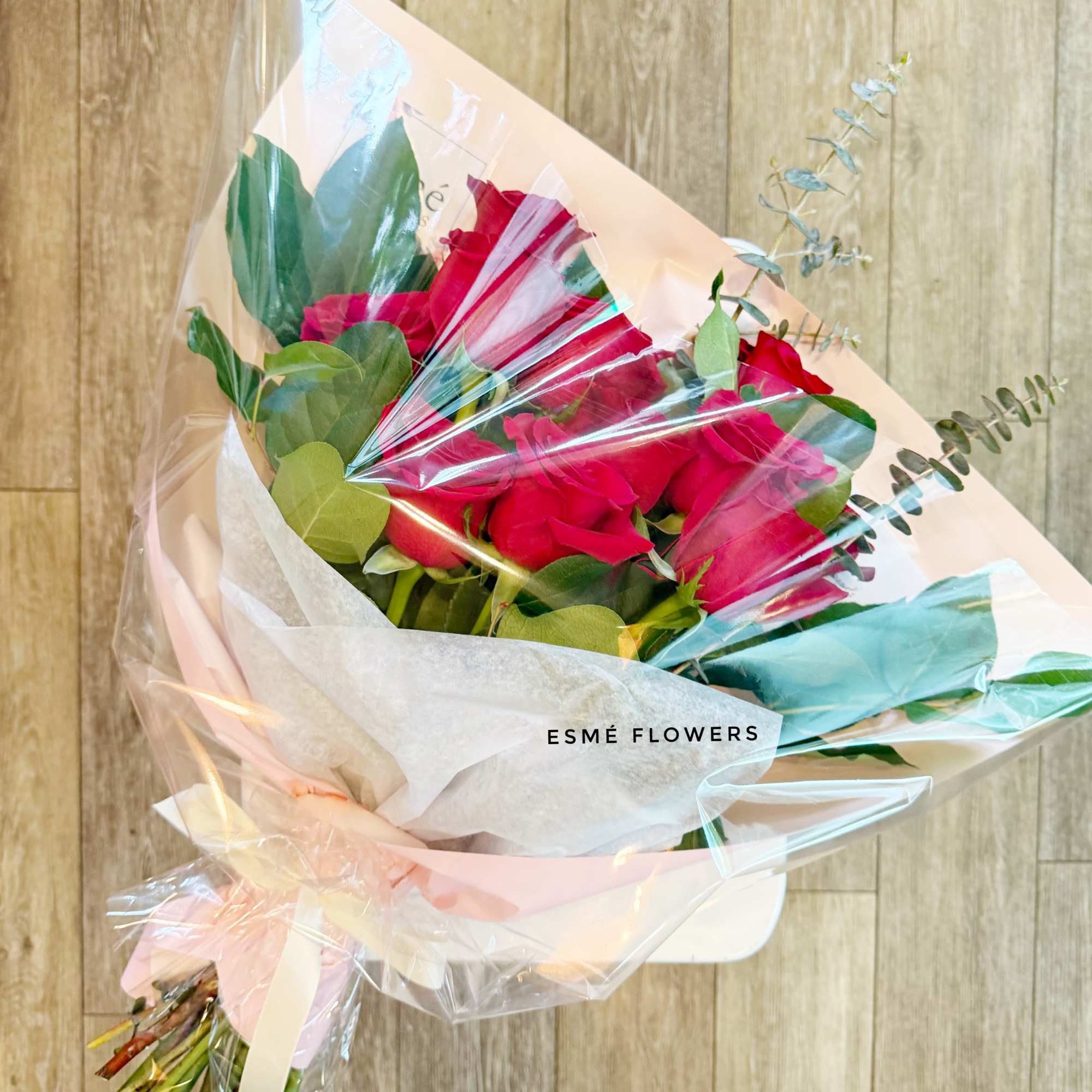 Bouquet of red roses wrapped in clear plastic with a pink ribbon