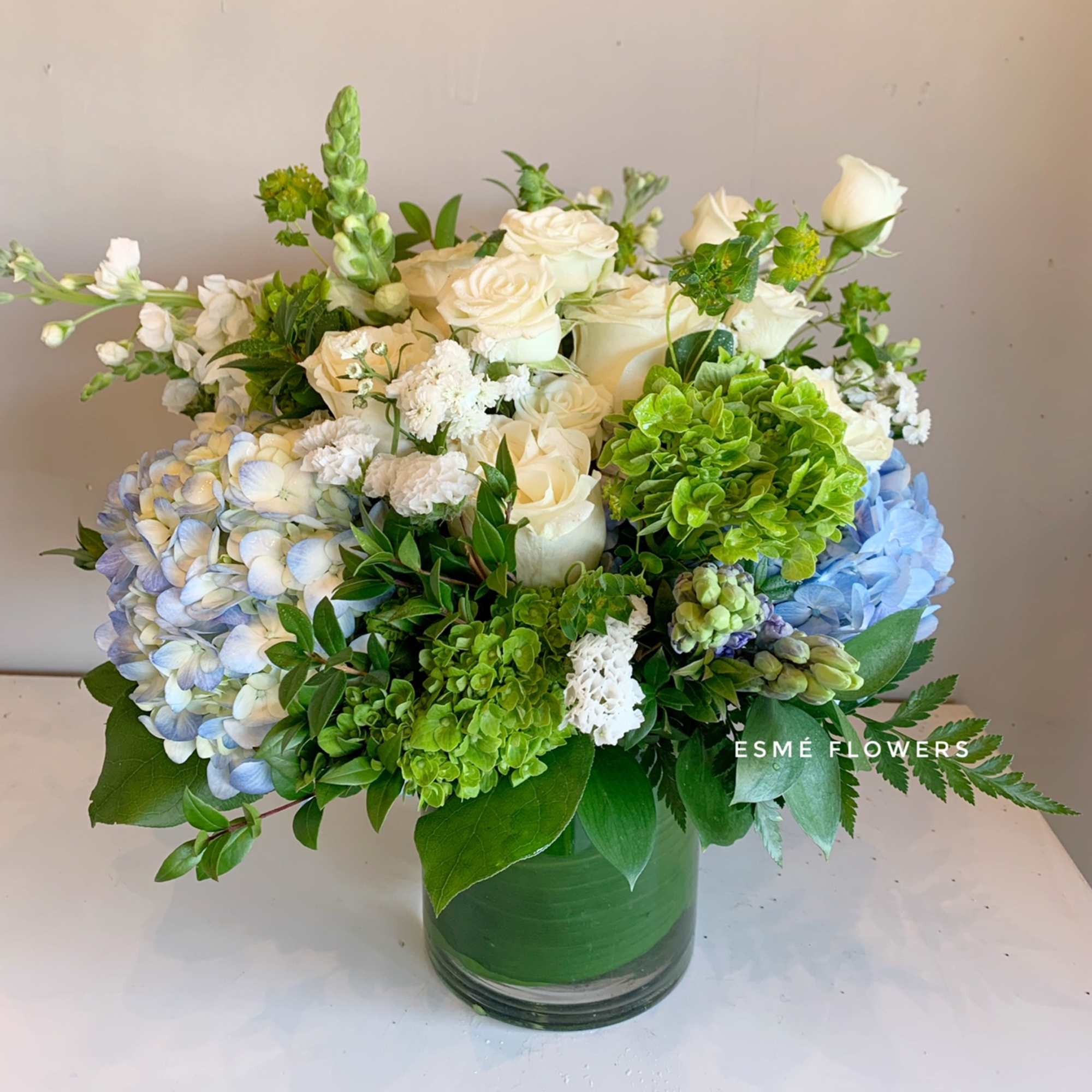 White roses and blue hydrangeas in a green glass vase