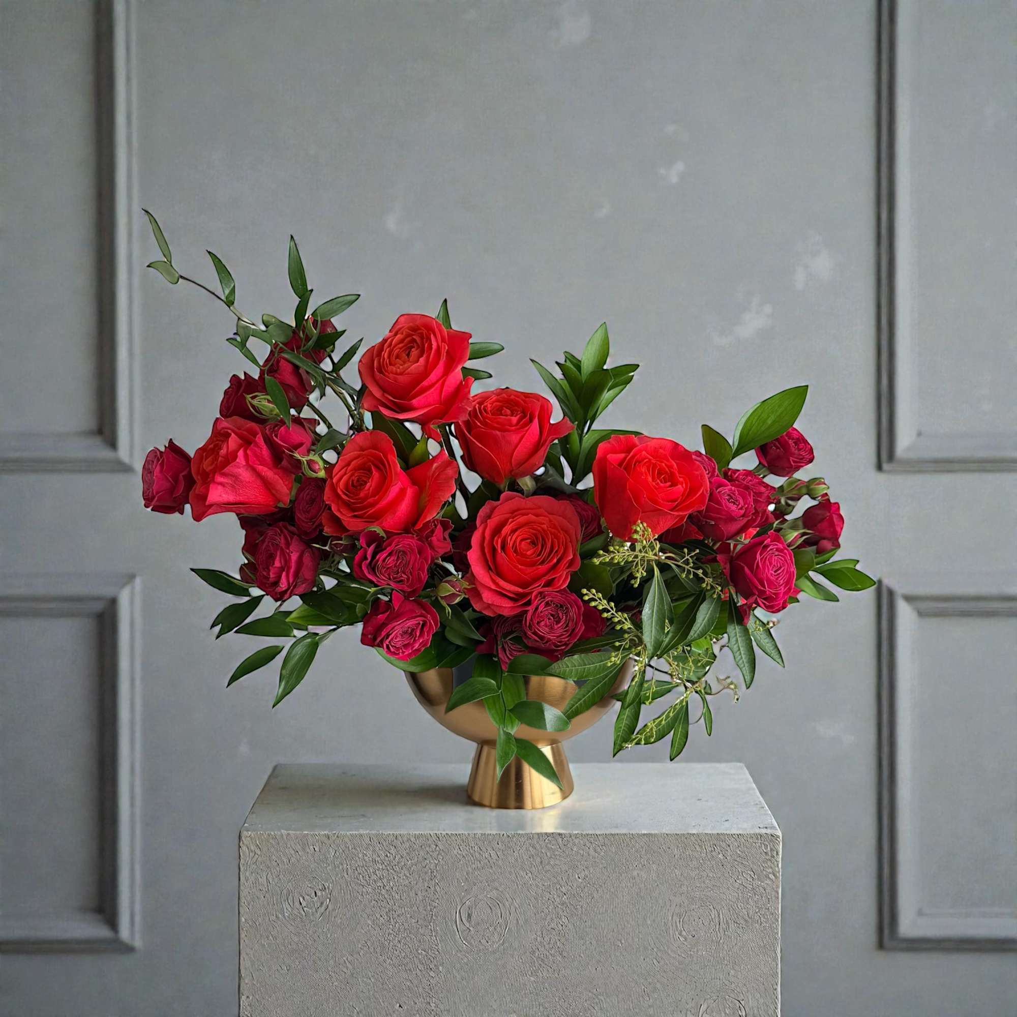 Red roses arranged in a gold vase with green foliage