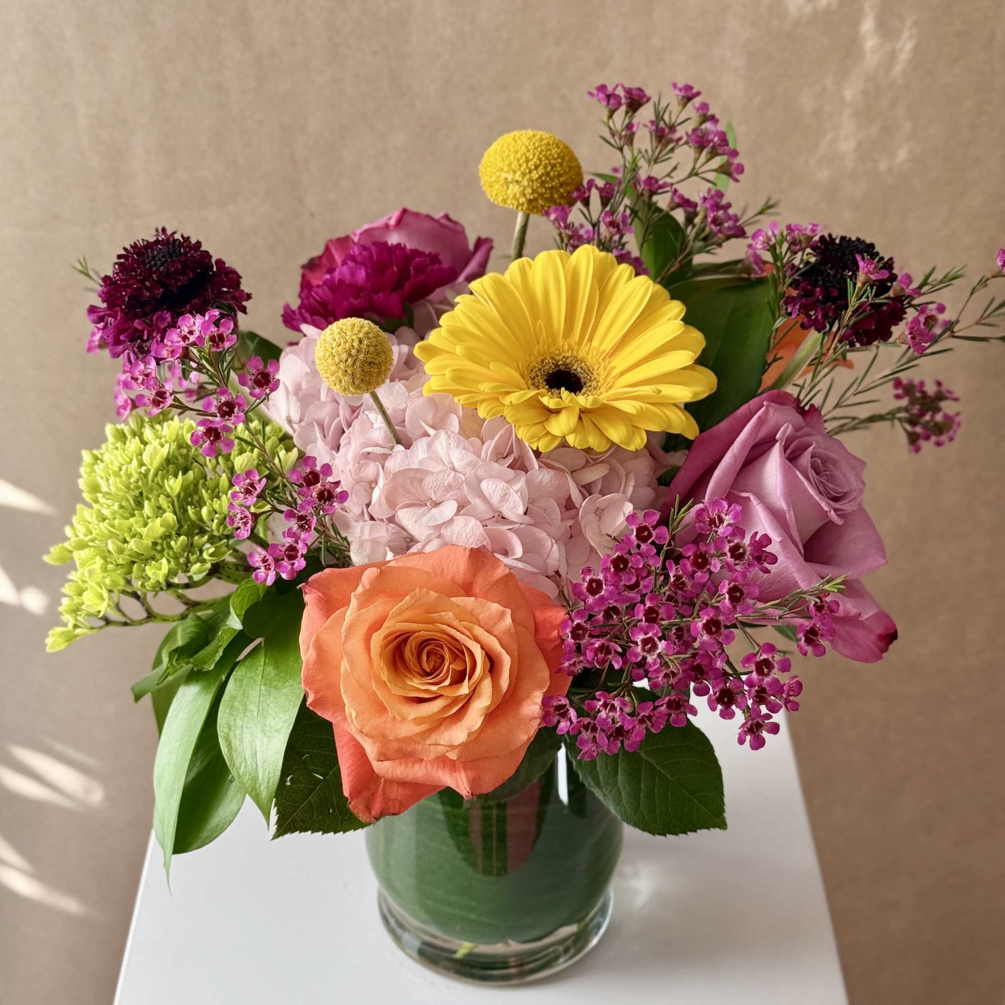 Mixed bouquet in a glass vase with roses, hydrangea, and bright yellow blooms