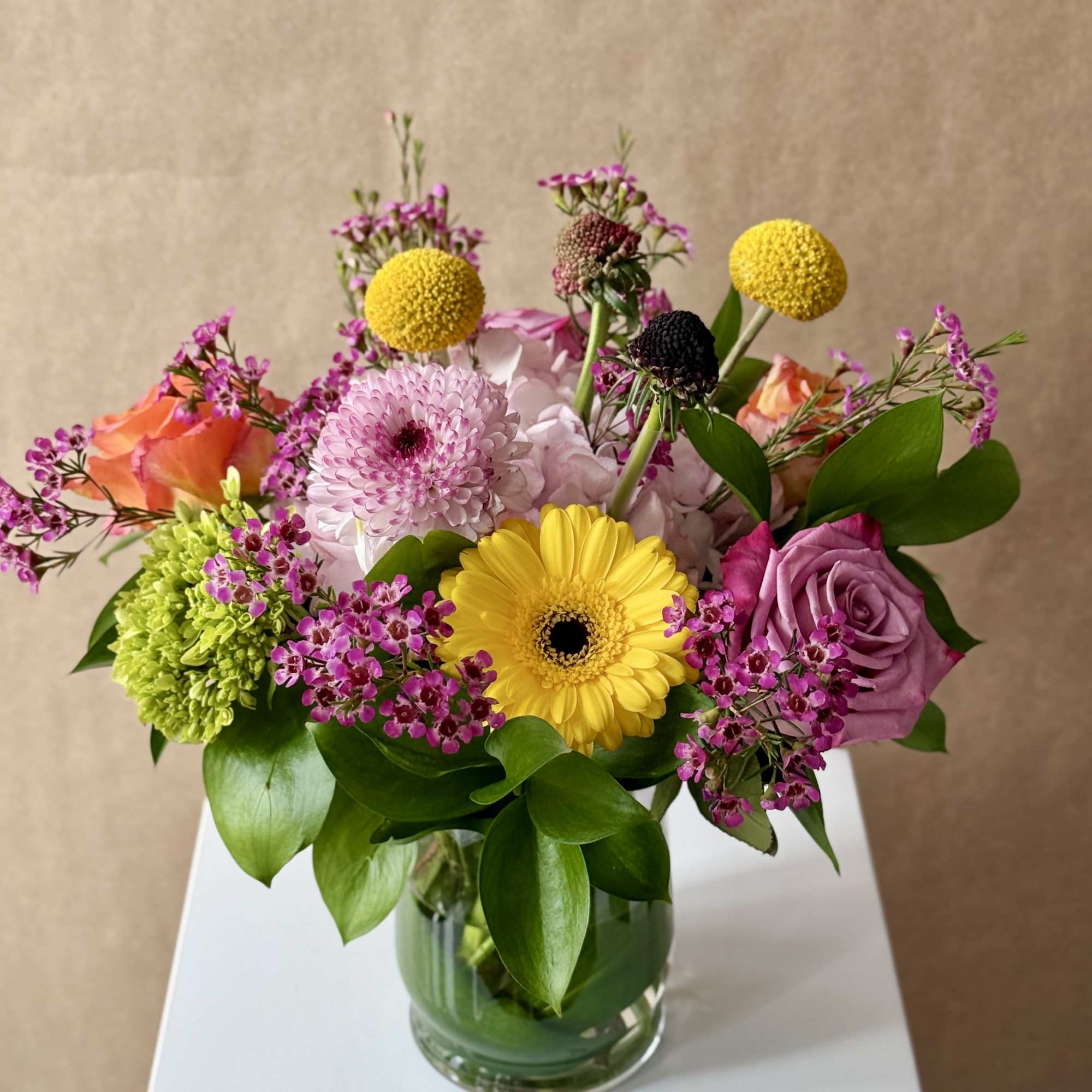 Mixed bouquet in a clear glass vase with roses, gerbera daisies, and button mums