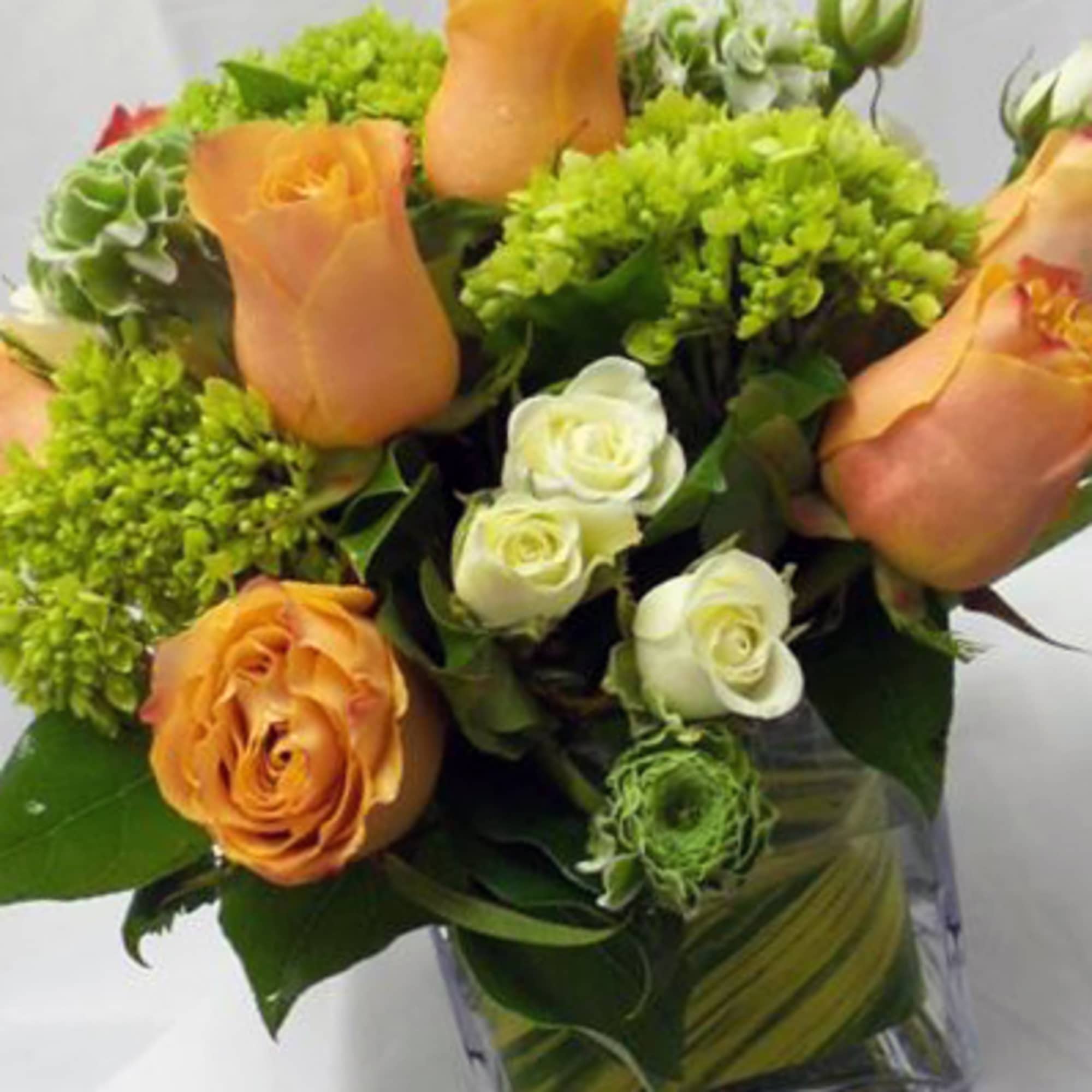 Bouquet of orange and white roses with green filler in a clear vase