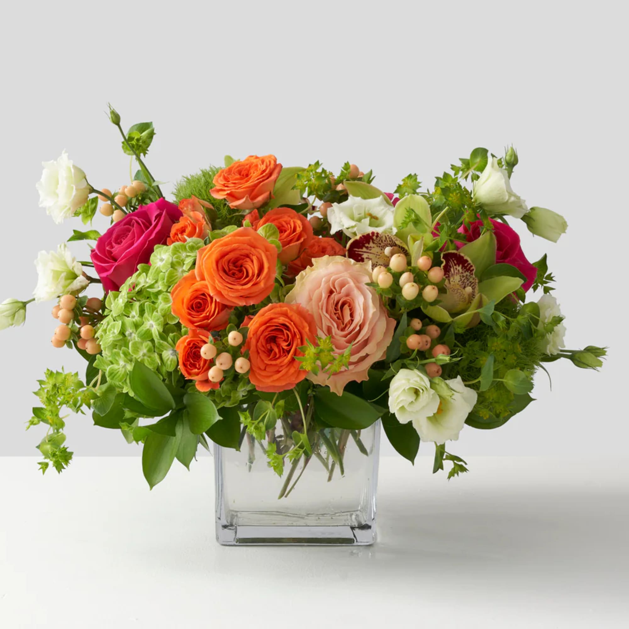 Mixed bouquet of orange, pink, and white roses in a clear glass vase