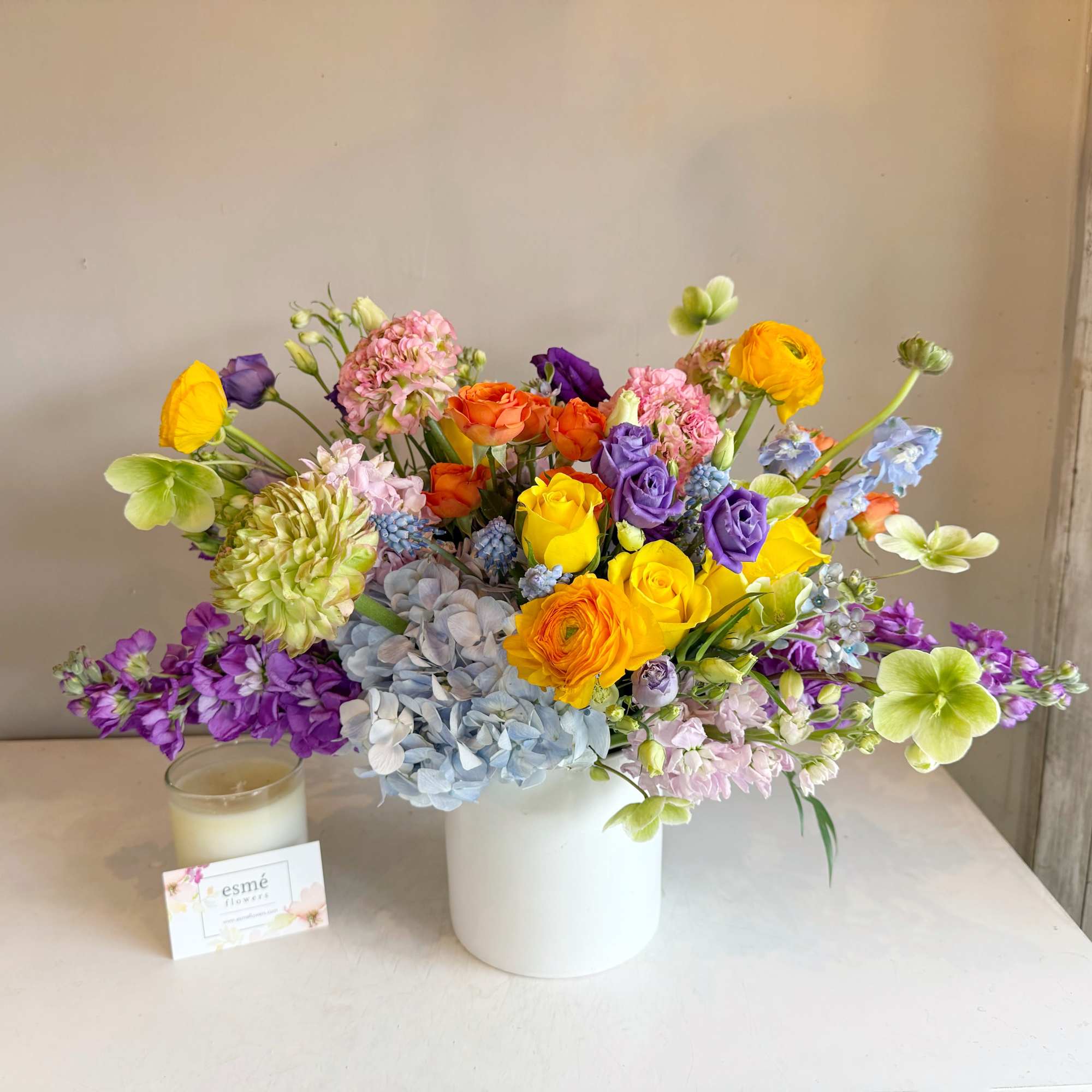 Colorful mixed bouquet in a white vase with a candle beside it