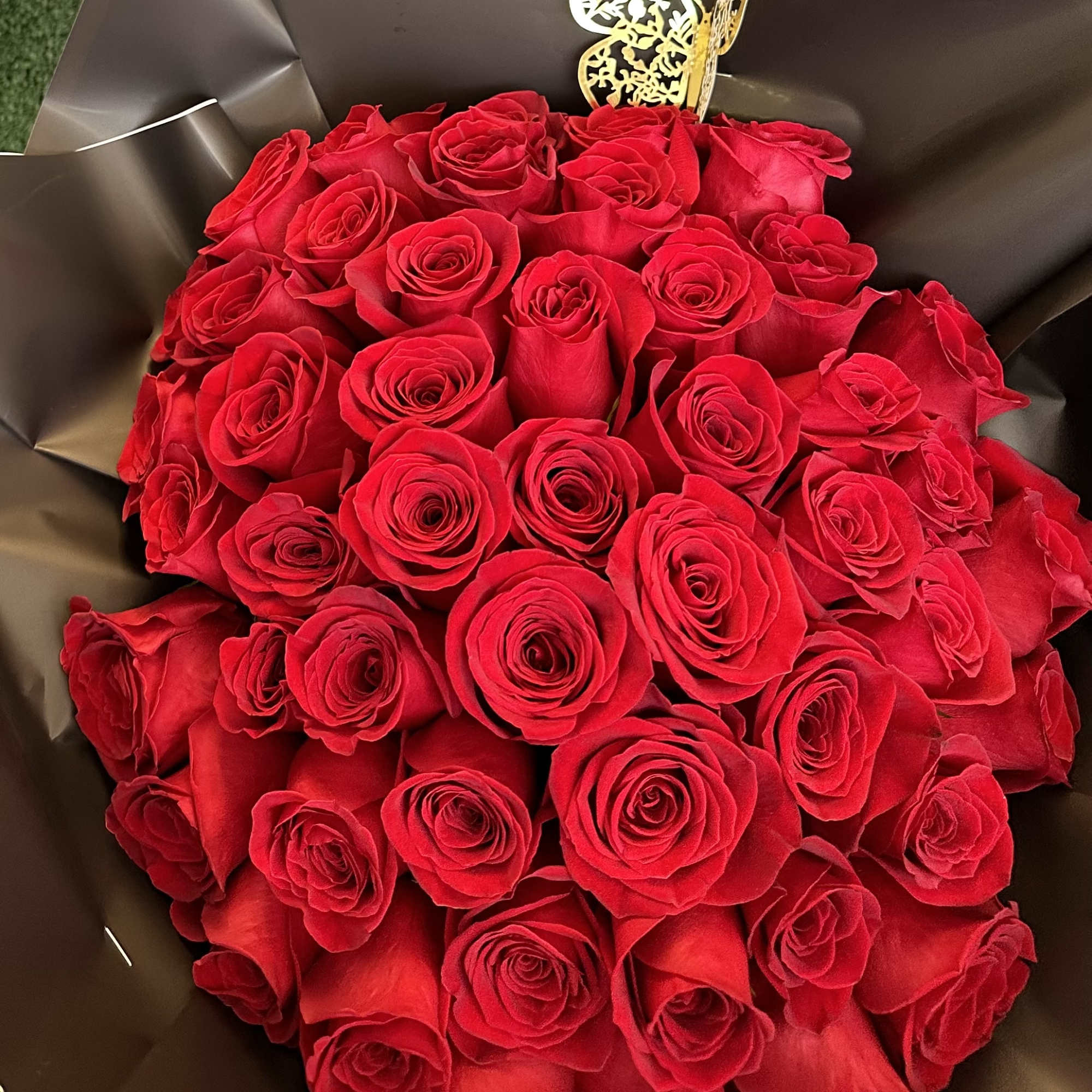 Bouquet of red roses wrapped in dark paper with a gold butterfly pick