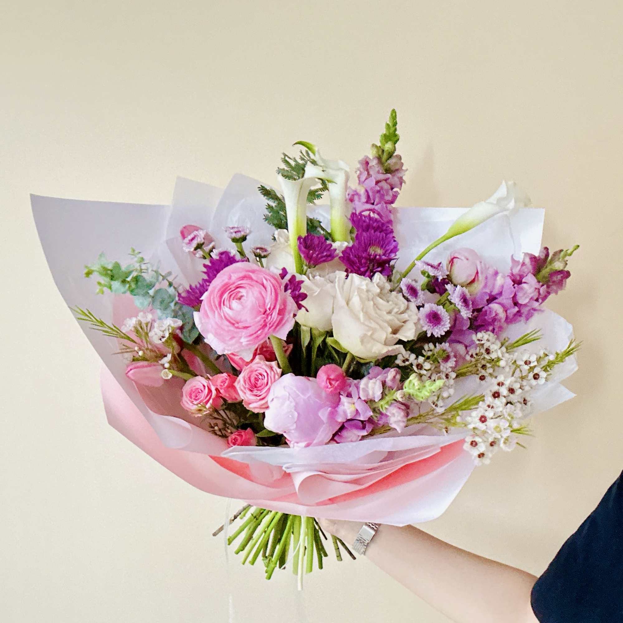 Handheld bouquet of pink and white flowers wrapped in pink paper