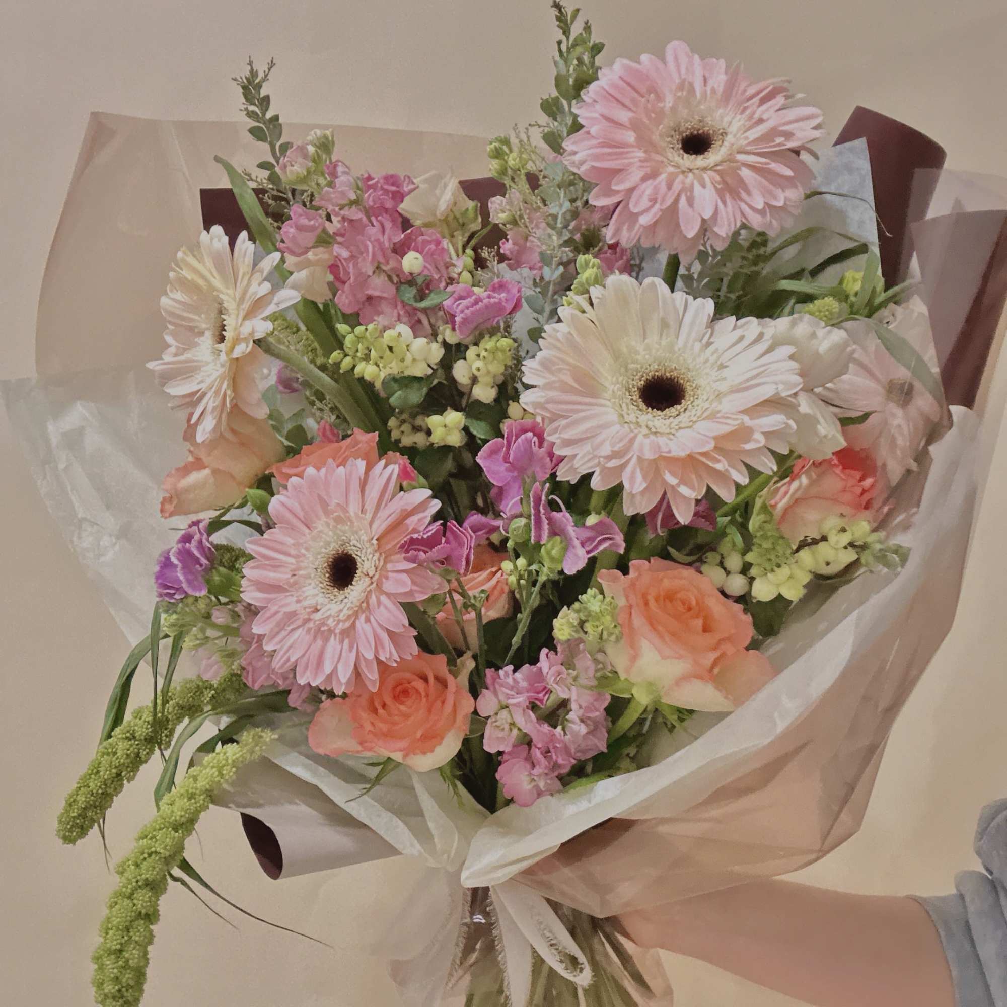 Handheld bouquet of pink gerbera daisies and peach roses wrapped in translucent paper